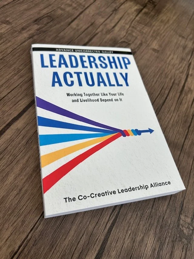 Book titled 'Leadership Actually' with a colorful arrow graphic on the cover, placed on a wooden surface.