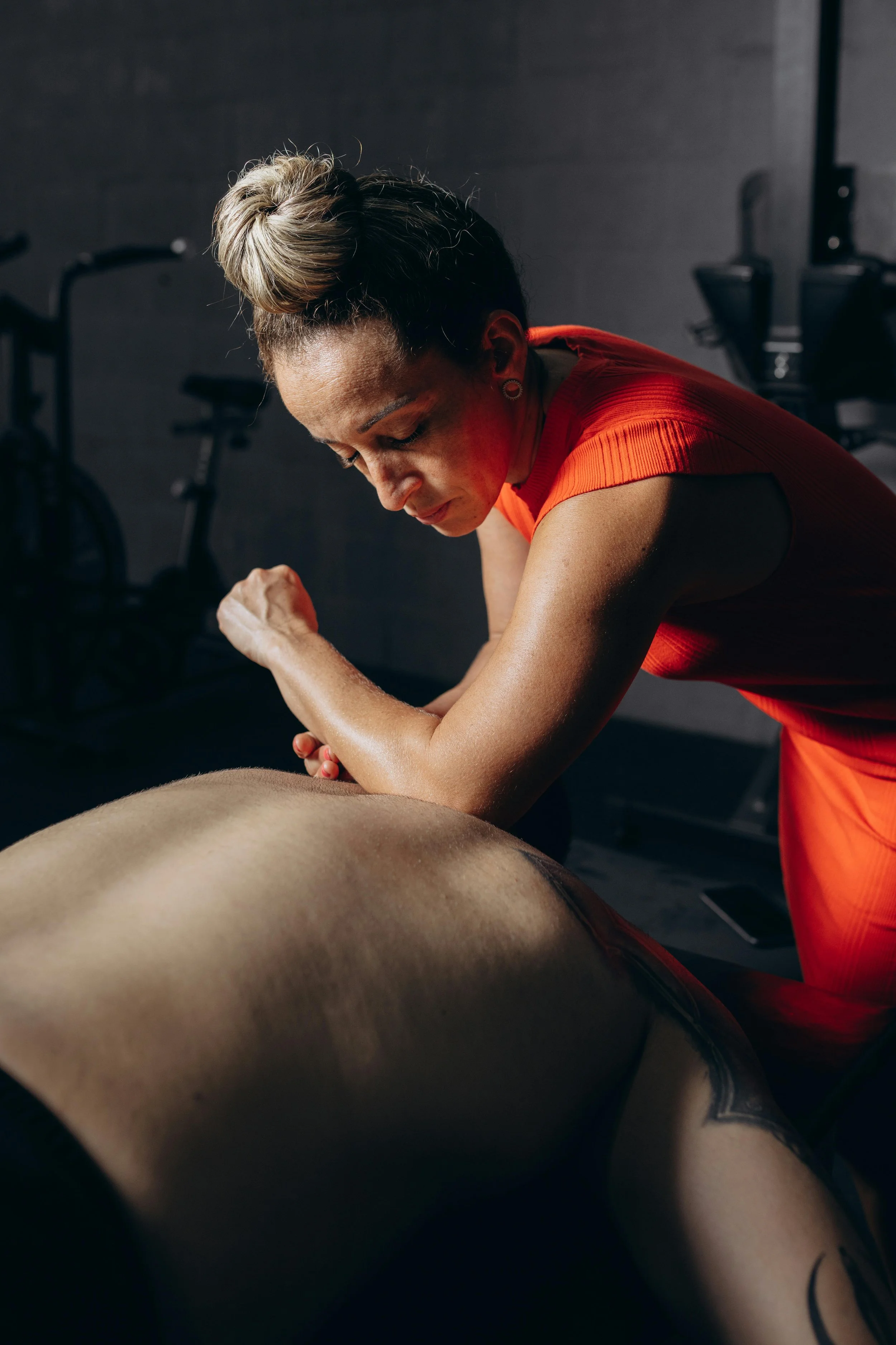 A woman in a red workout outfit giving a massage to a man lying face down on a massage table in a gym.