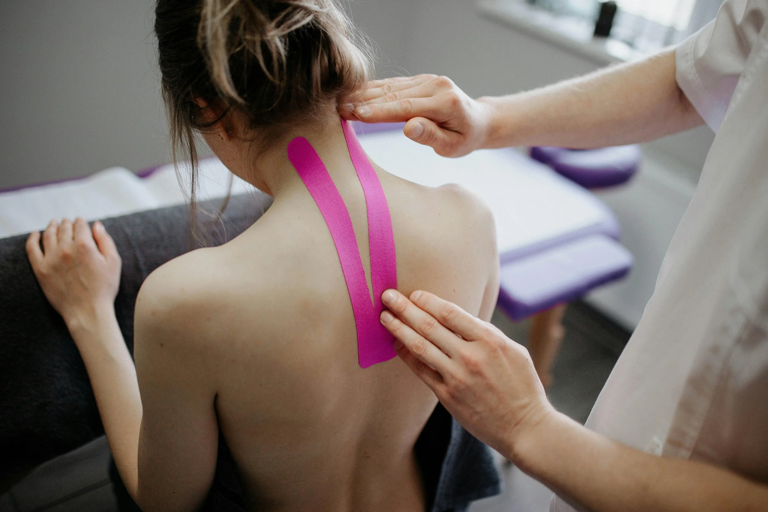 A woman with dark hair receiving a cupping therapy session on her back using pink adhesive cups.