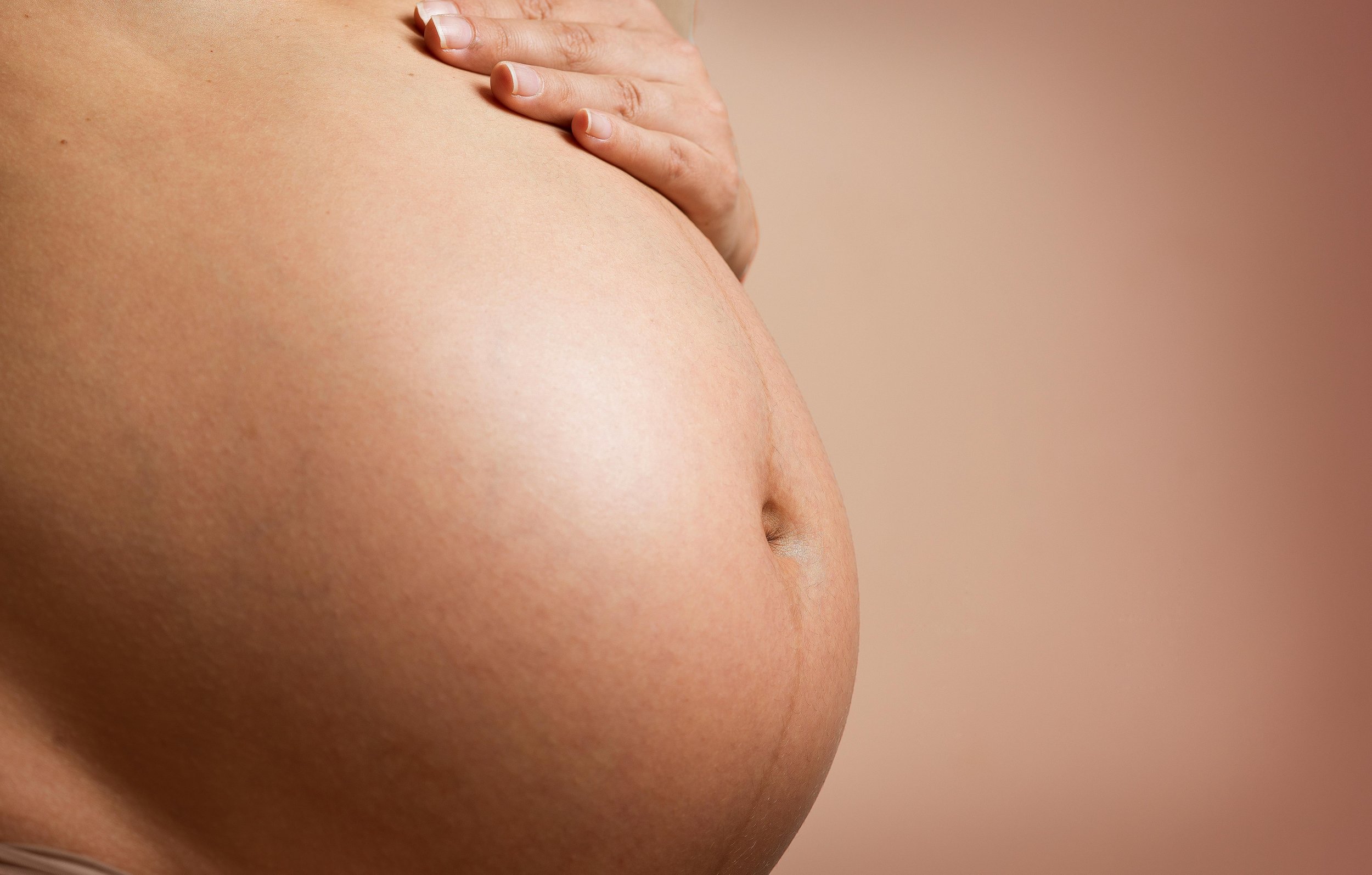 Close-up of a pregnant belly with a hand resting on it, against a warm-toned background.