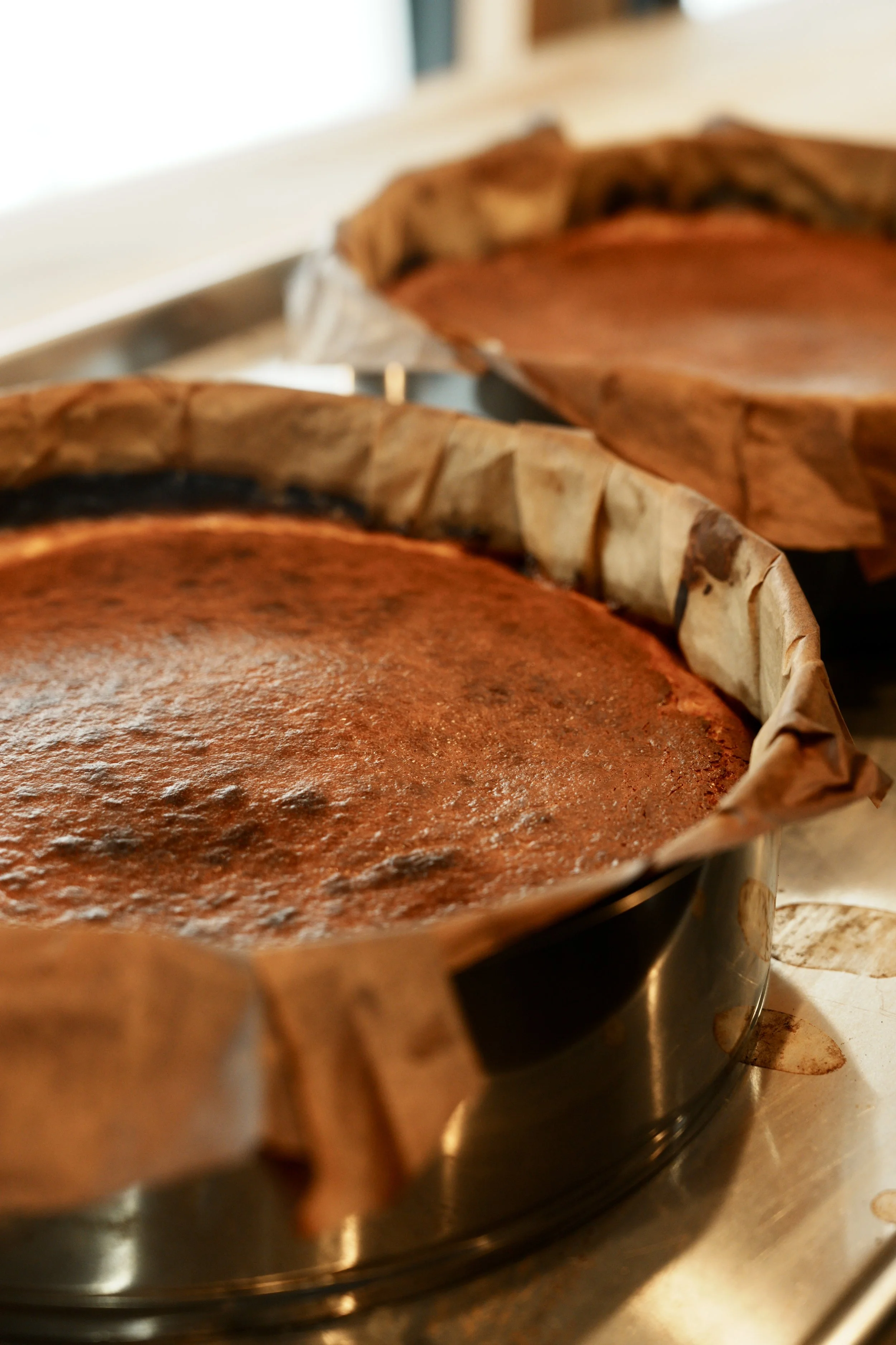 Two baked cakes in round pans with parchment paper, cooling on a countertop.