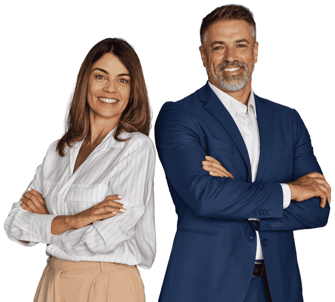 A man and woman standing side by side with arms crossed, smiling, dressed in business attire. The woman has shoulder-length brown hair, wearing a white blouse and beige pants. The man has gray hair and a beard, wearing a blue suit with a white shirt.