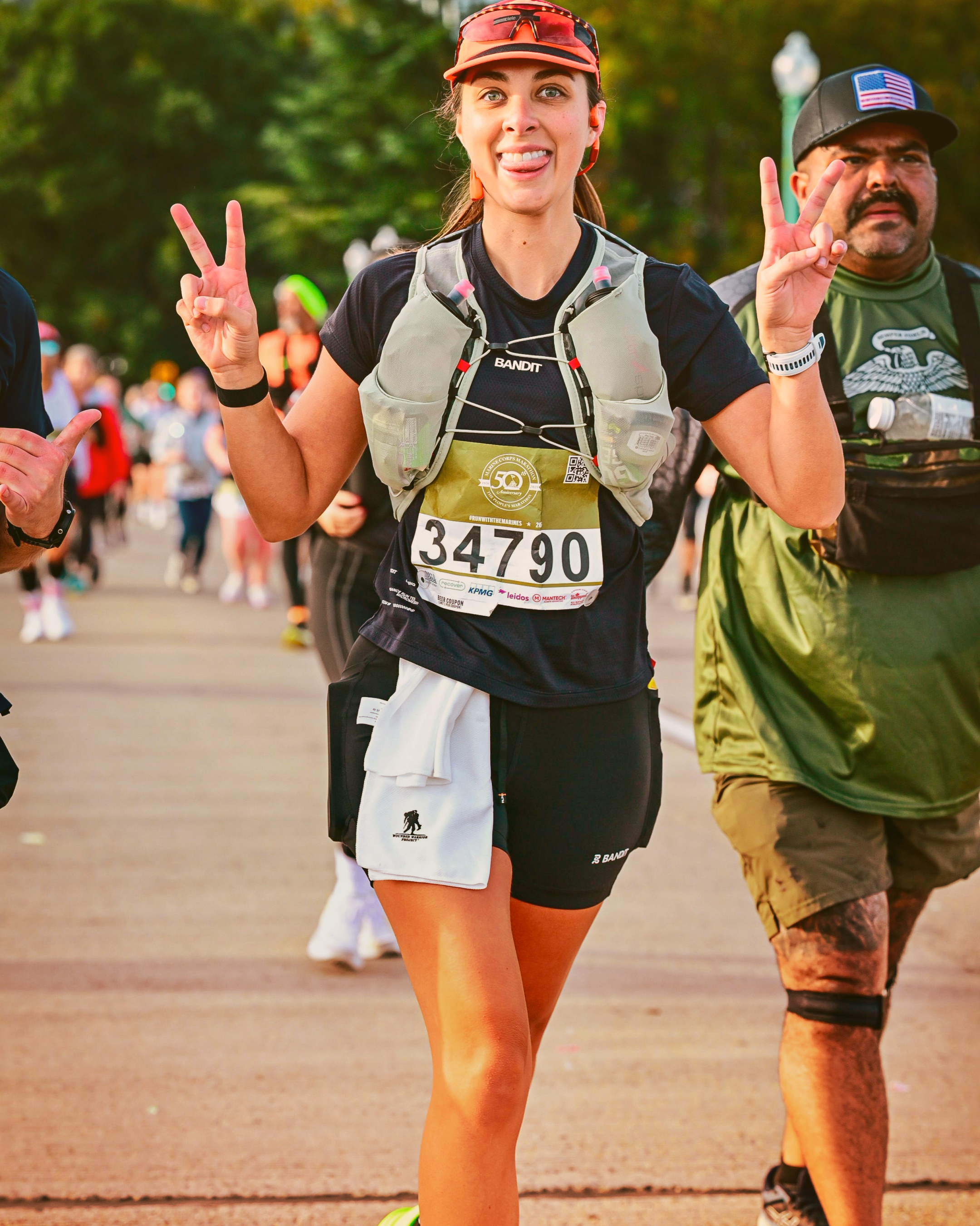A group of people, including a young woman in the foreground wearing a black long-sleeve shirt and a black cap, standing on a dirt path outdoors during daytime.