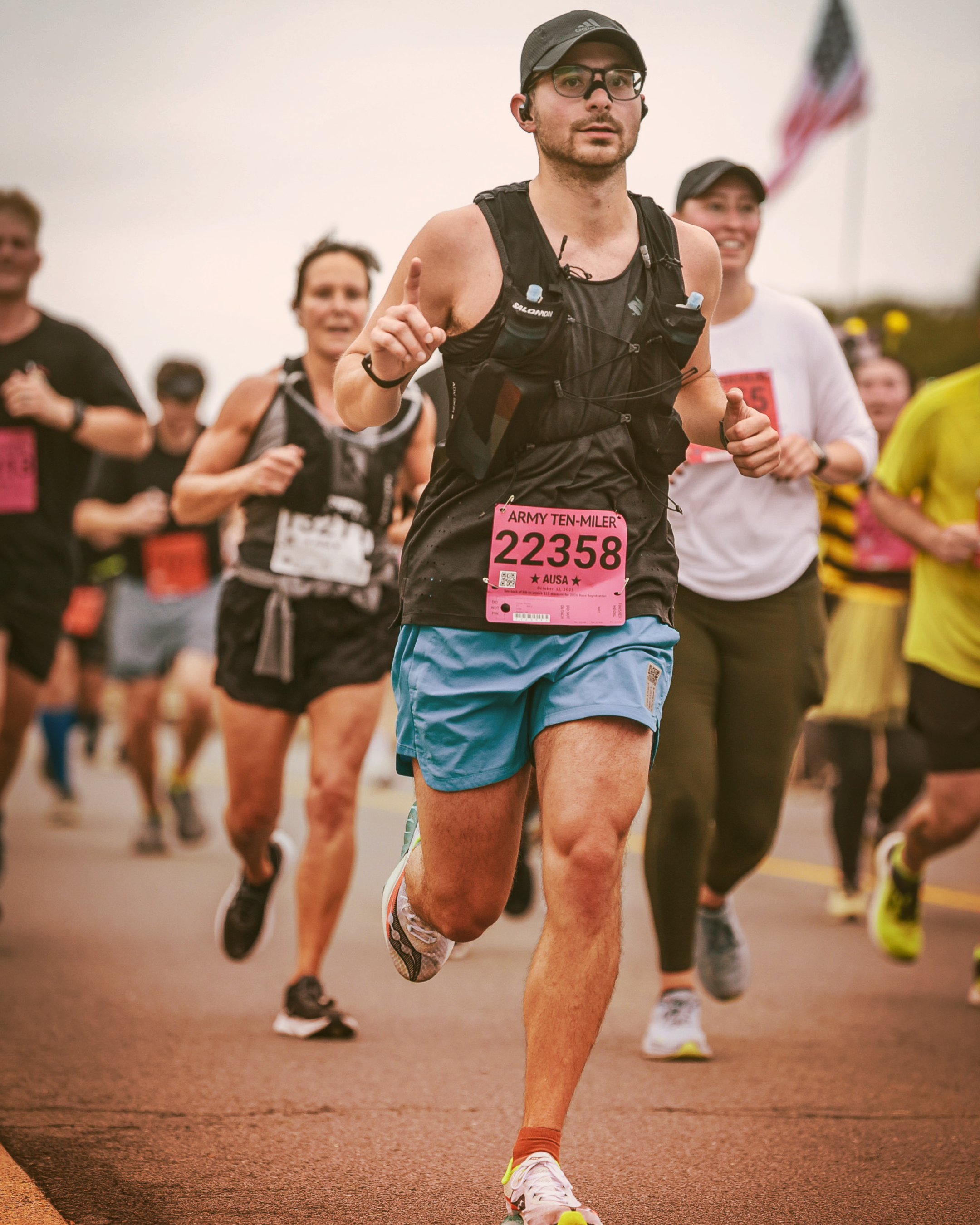 A man sitting on white chairs with blue covers at the MUBADALA CITY DC OPEN tennis event, wearing a white sun hat, black sunglasses, a light-colored short-sleeve shirt, black shorts, and holding a smartphone.