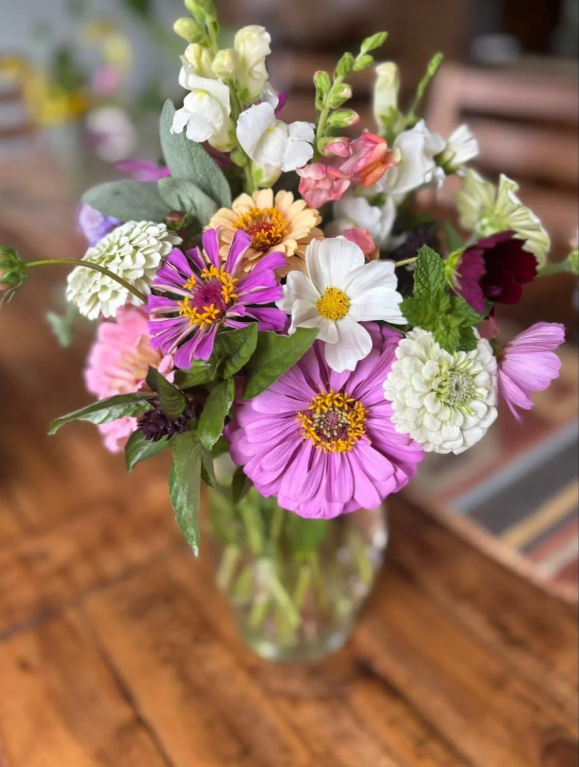 A colorful bouquet of mixed flowers in a glass vase on a wooden table.