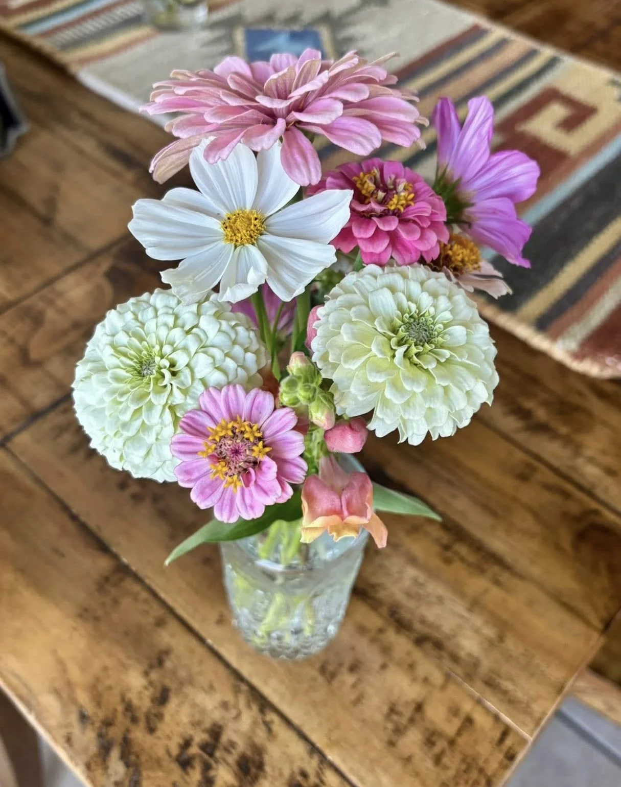 A bouquet of pink, white, and purple flowers in a glass vase on a wooden table.