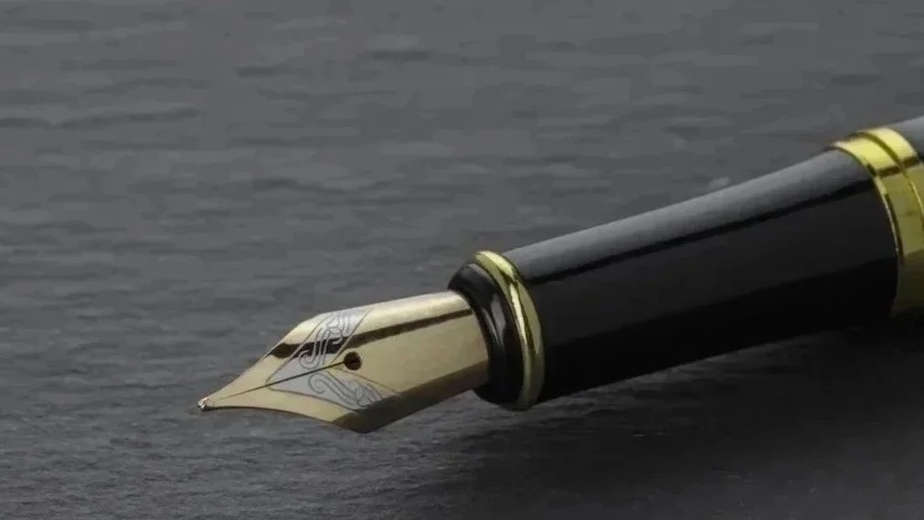 Close-up of a black and gold fountain pen on a dark surface.