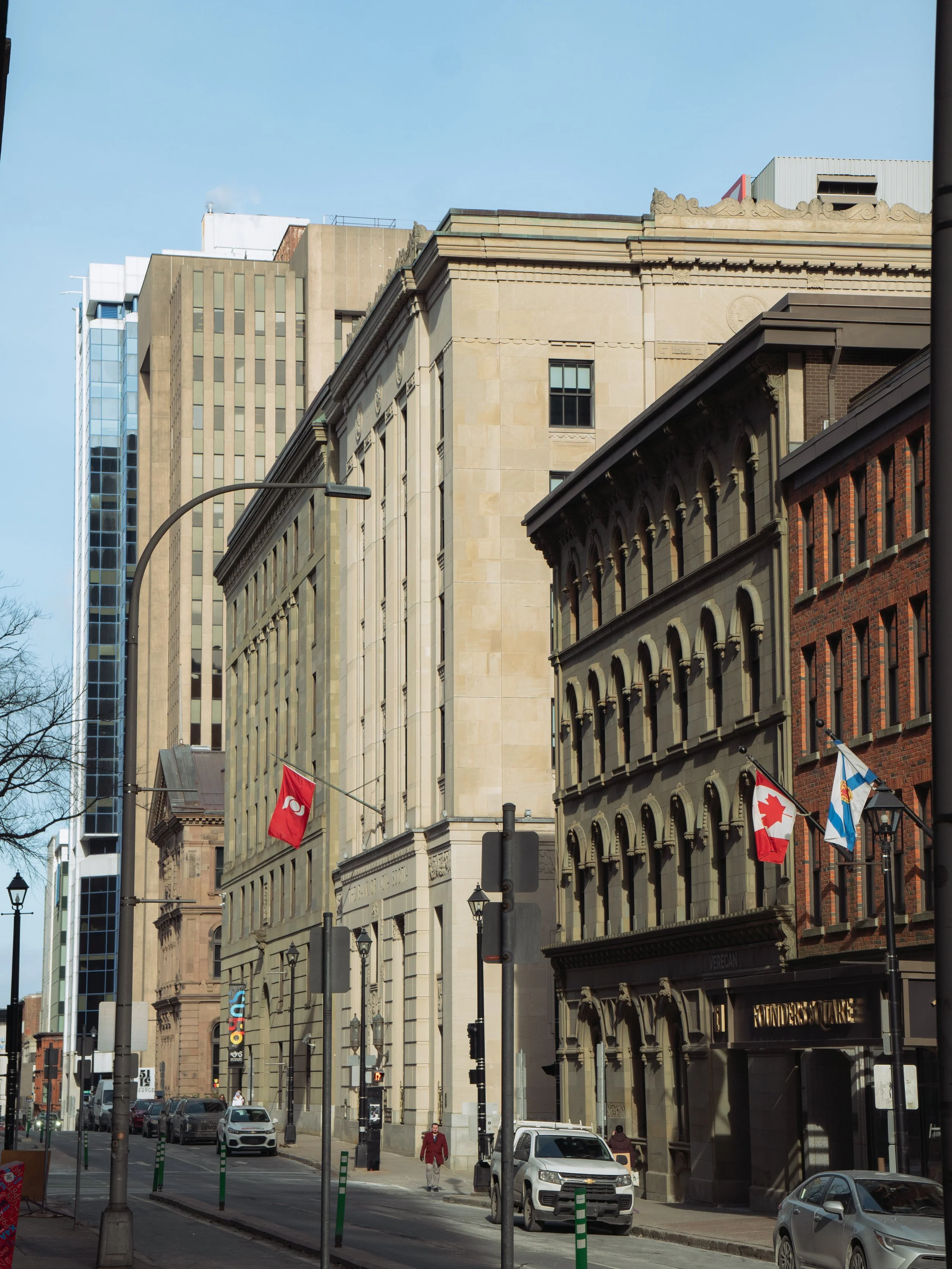 Halifax Nova Scoria. City street view with historic and modern buildings, Canadian and Ontario flags, street lamps, parked cars, and pedestrians. Shows off the area for MLS listing. 