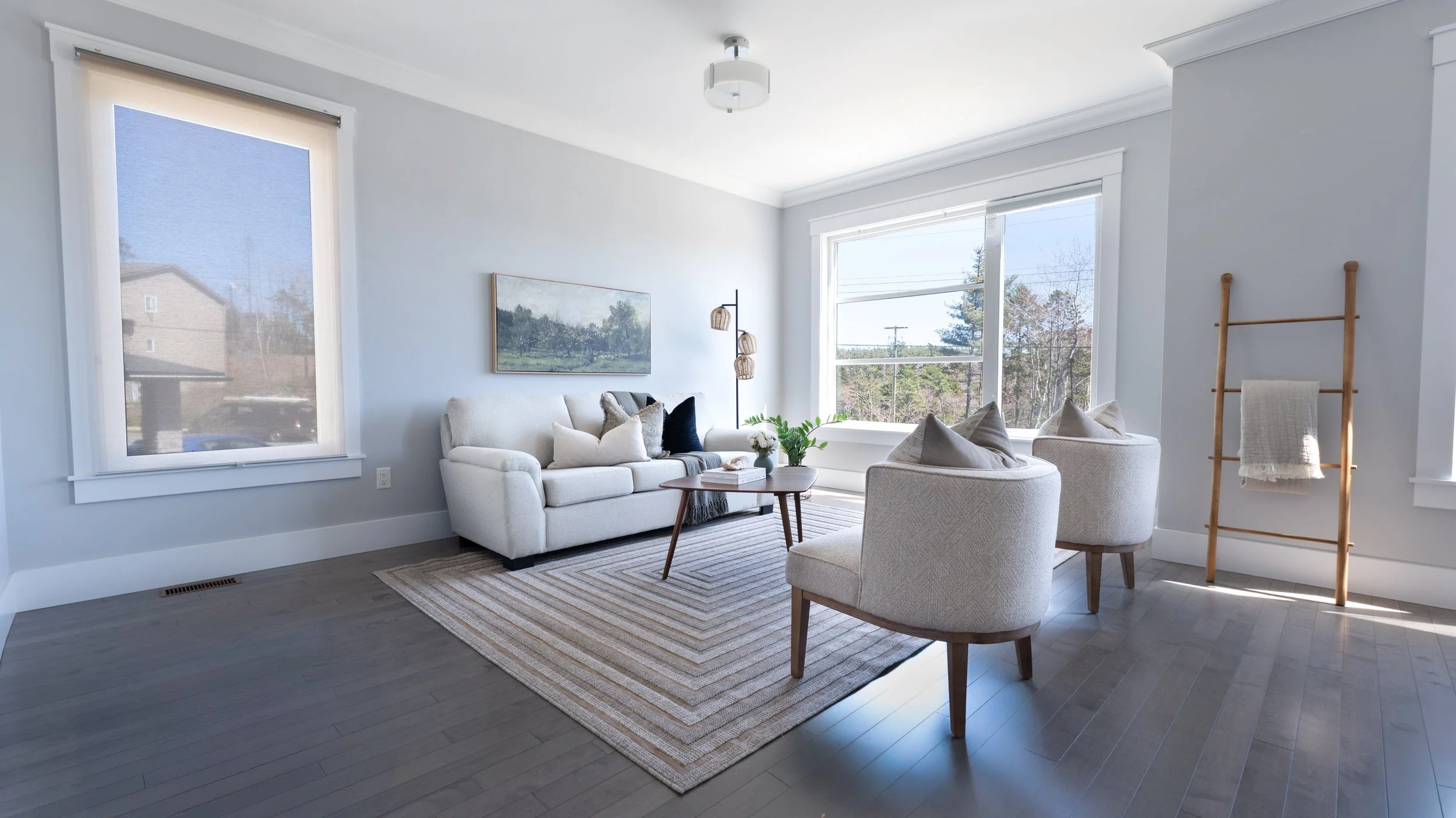 Professional high quality Halifax Nova Scotia real estate photography. MLS Listing Photo. Bright living room with large windows, white sofa, two white armchairs, wooden coffee table, framed artwork, area rug, and a ladder with a towel.