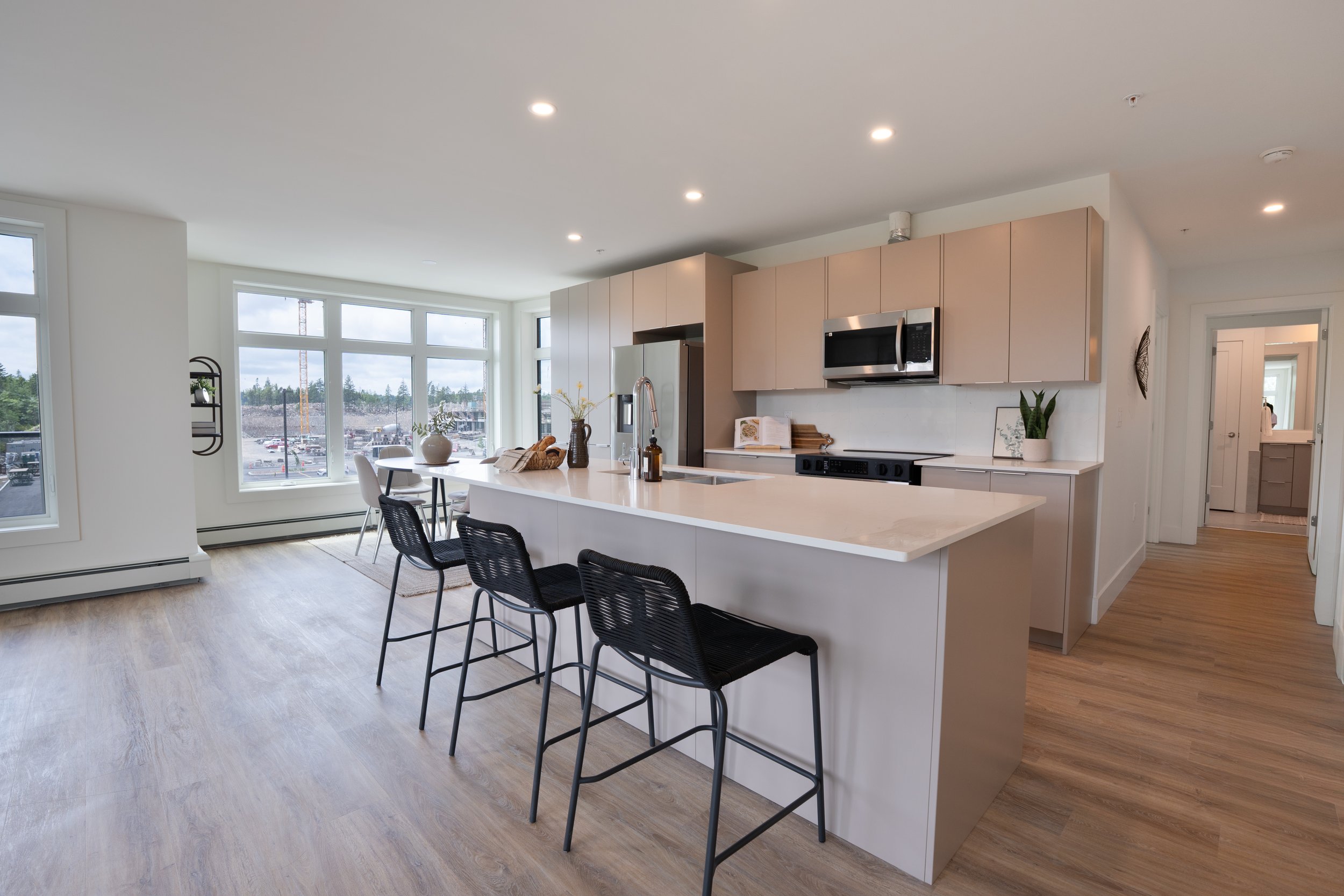 Professional high quality Halifax Nova Scotia real estate photography. MLS Listing Photo. Modern kitchen with white countertops, beige cabinets, black bar stools, stainless steel appliances, and large windows