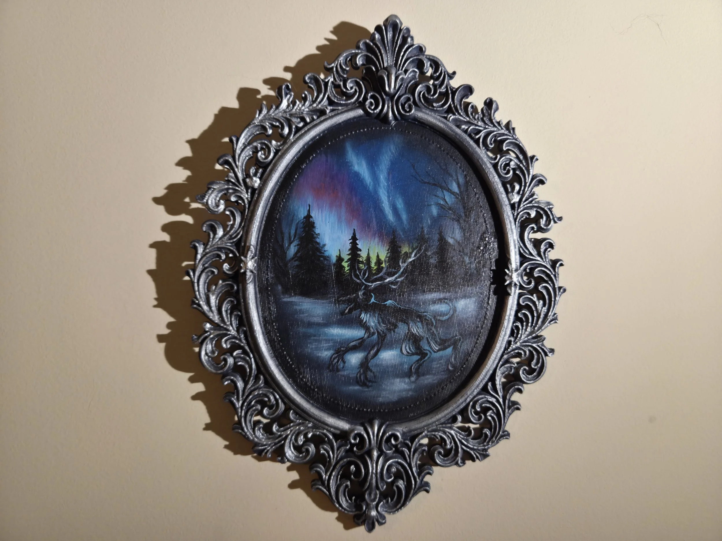Painting of a mythical creature, a wolf with antlers, standing in a snowy landscape with pine trees, under a colorful night sky with aurora borealis, framed in an ornate metallic frame.