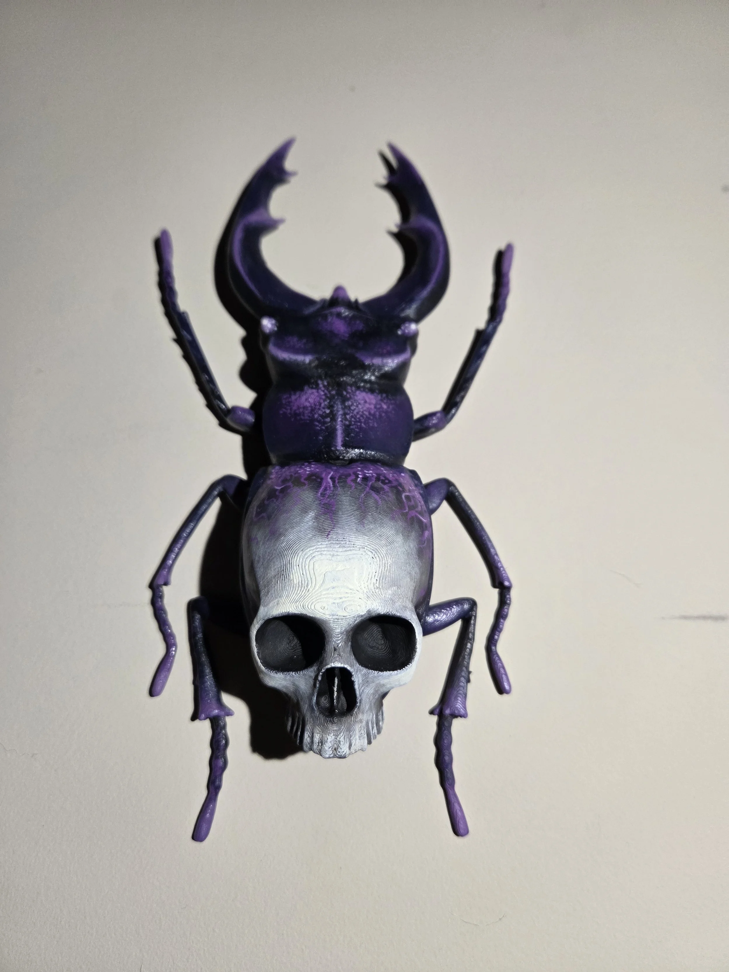 A decorative object resembling a combination of a purple beetle and a human skull, with a purple body and black details, placed on a light-colored surface.
