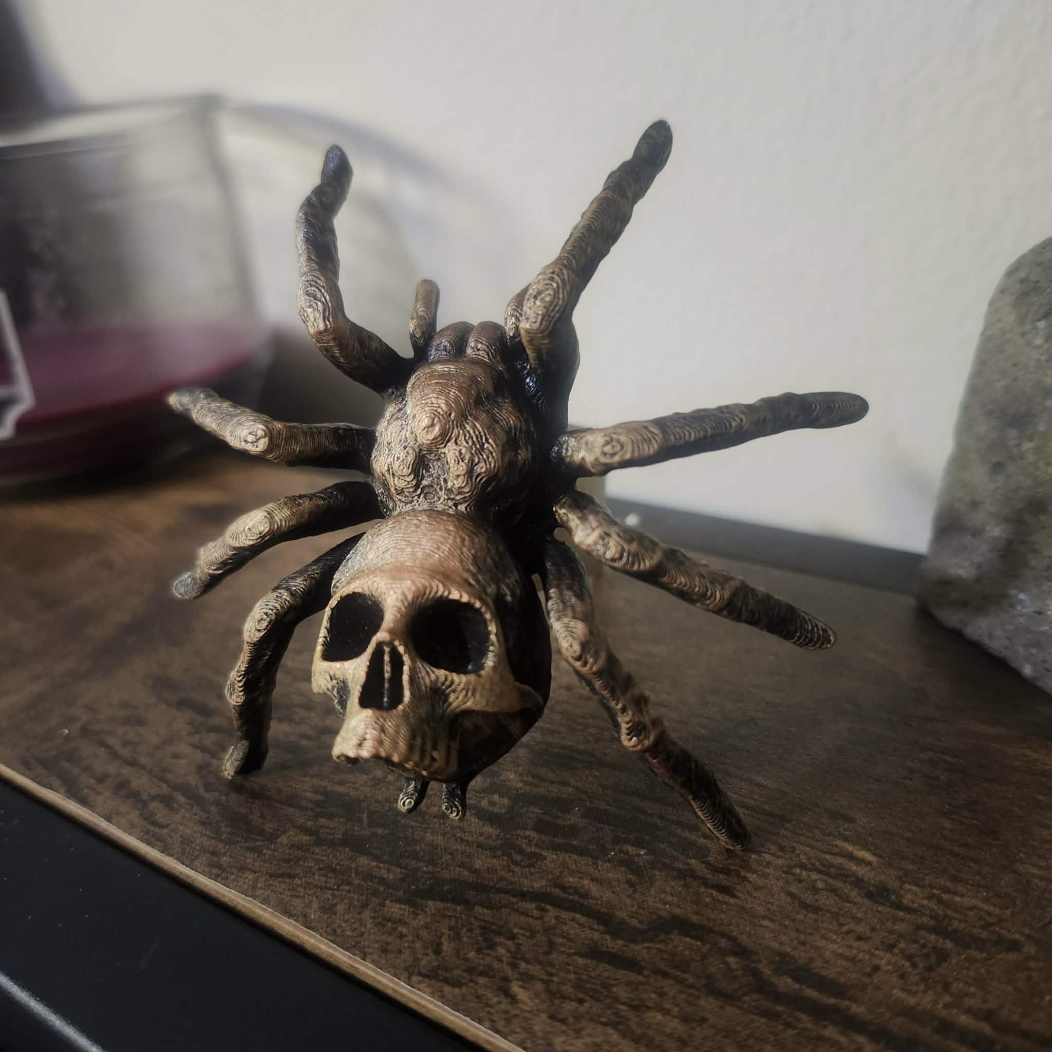 A decorative sculpture combining a spider with a skull, featuring a detailed skull face with eye sockets and a textured spider body and legs.