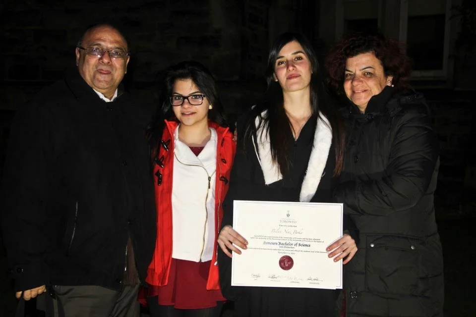 A young woman holding a diploma standing with three older adults outdoors at night, celebrating her graduation.