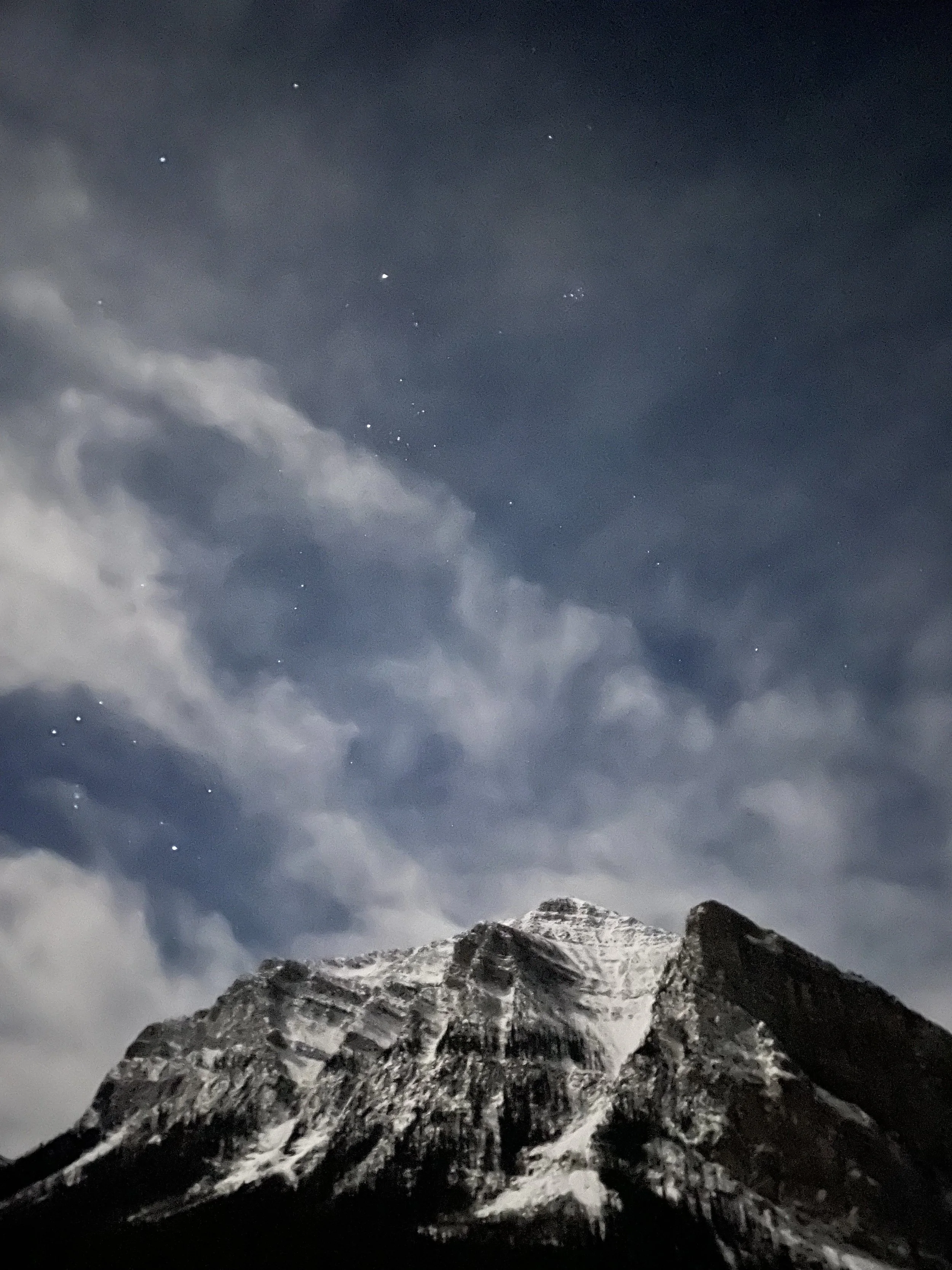 Nighttime view of a snow-capped mountain with a cloudy sky and visible stars.