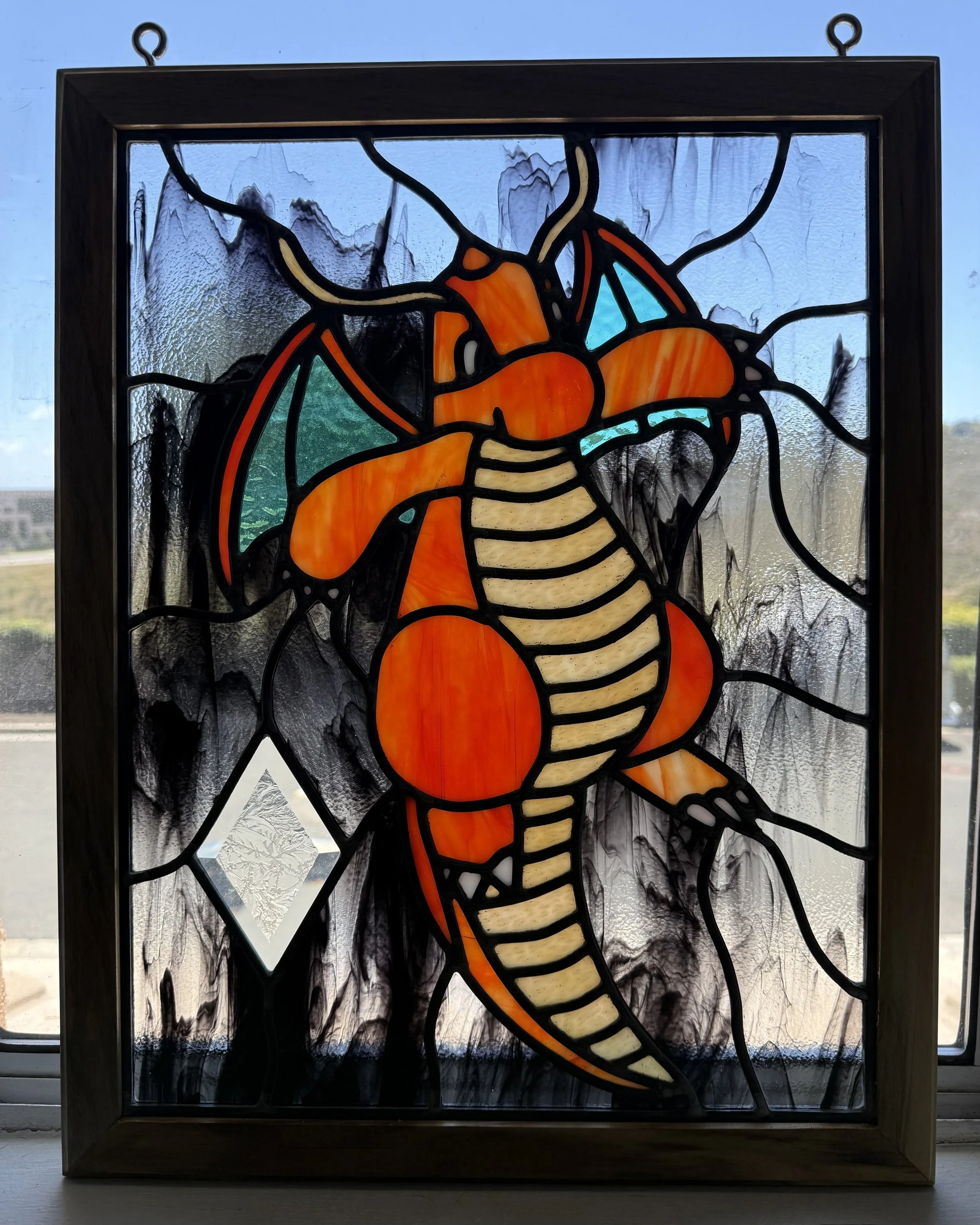 A framed stained glass artwork of a colorful lobster, with black outlines, set against textured glass background.