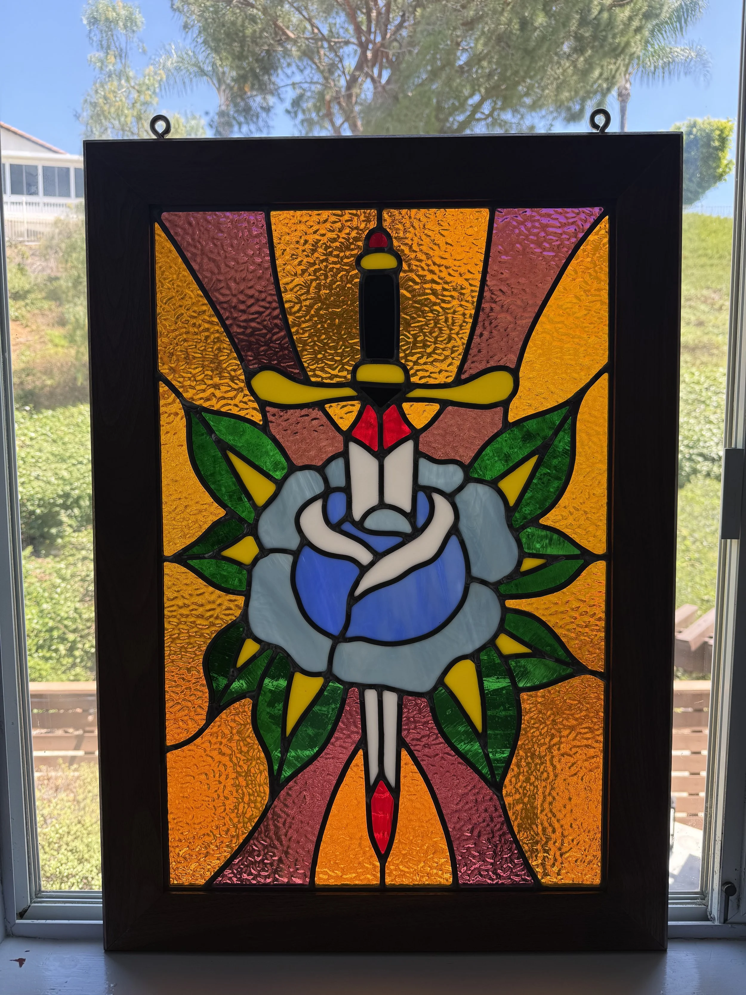 Colorful stained glass window depicting a rose and dagger, and a background of orange textured glass.