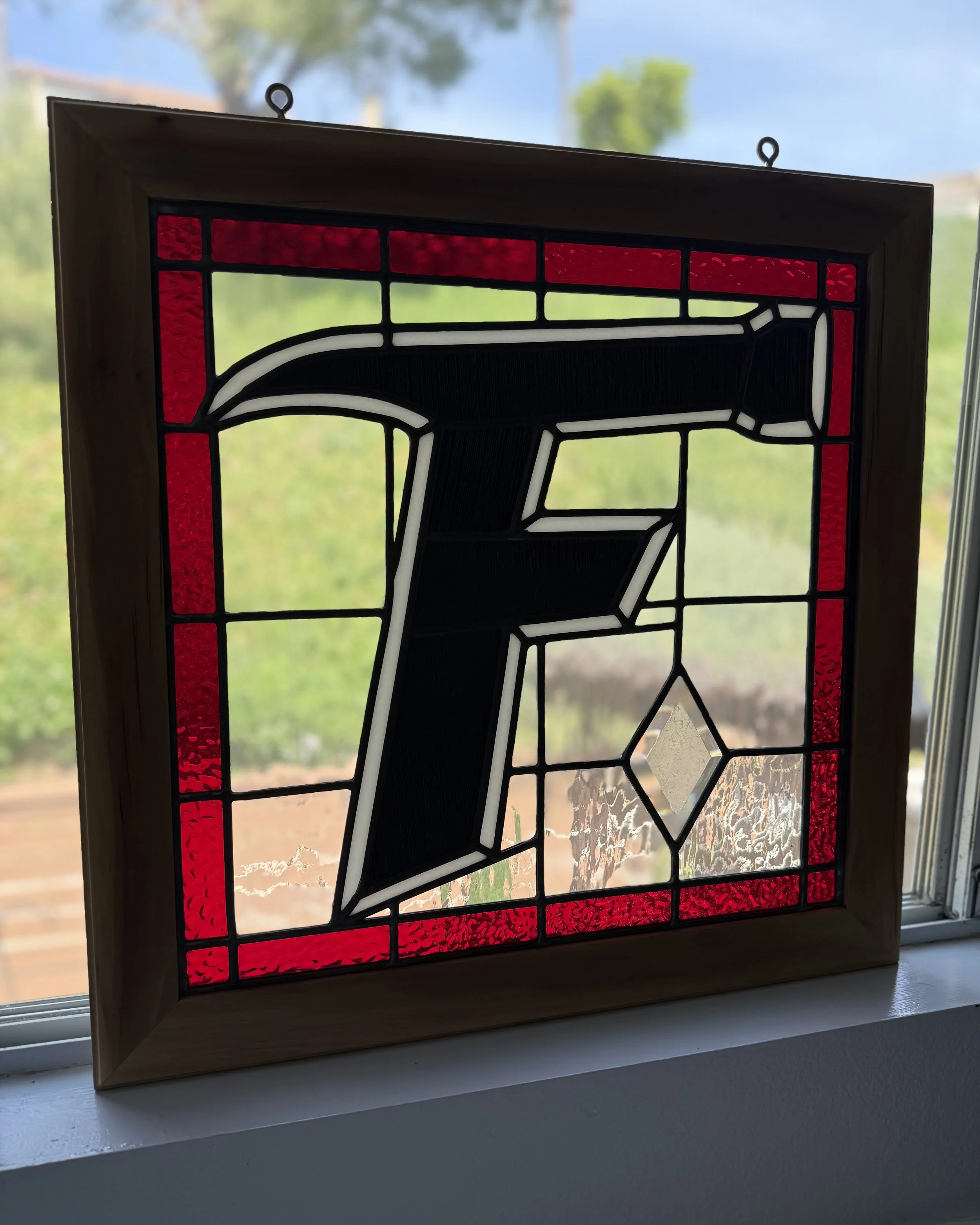 Stained glass window with the letter "F" in black, surrounded by red glass and a wooden frame.