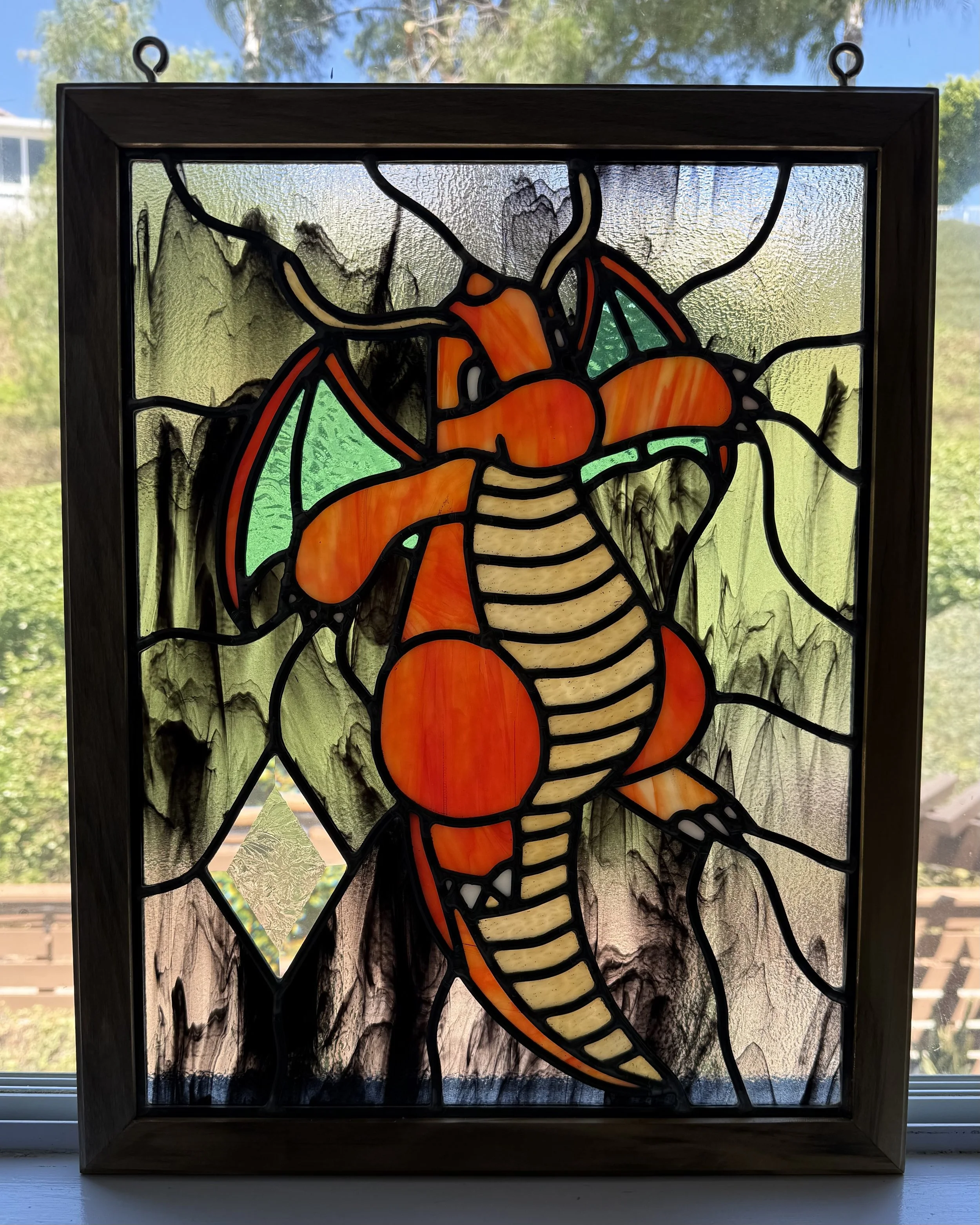 Stained glass window depicting a lobster with orange and cream colors, framed in black and wood, backlit by natural light.