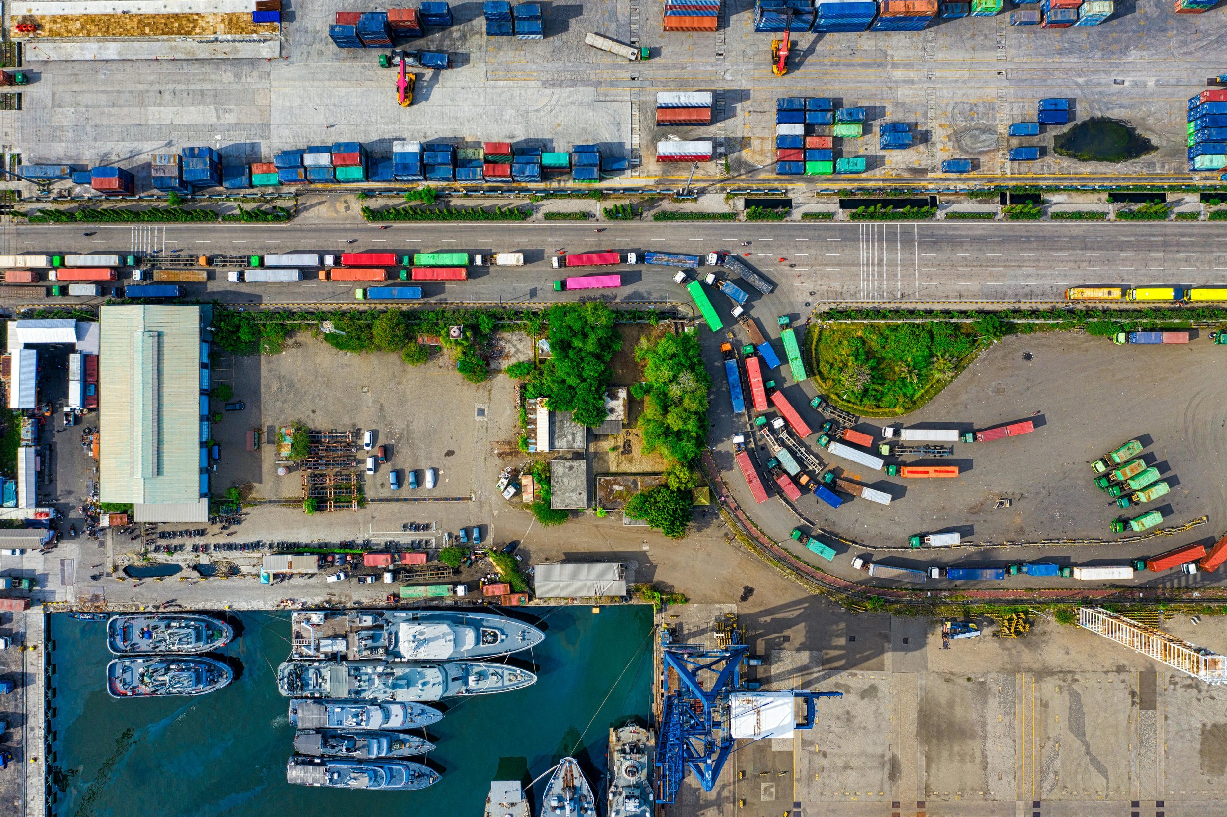 Aerial view of shipping containers and cargo trucks in port, illustrating the global circulation of goods and desire.