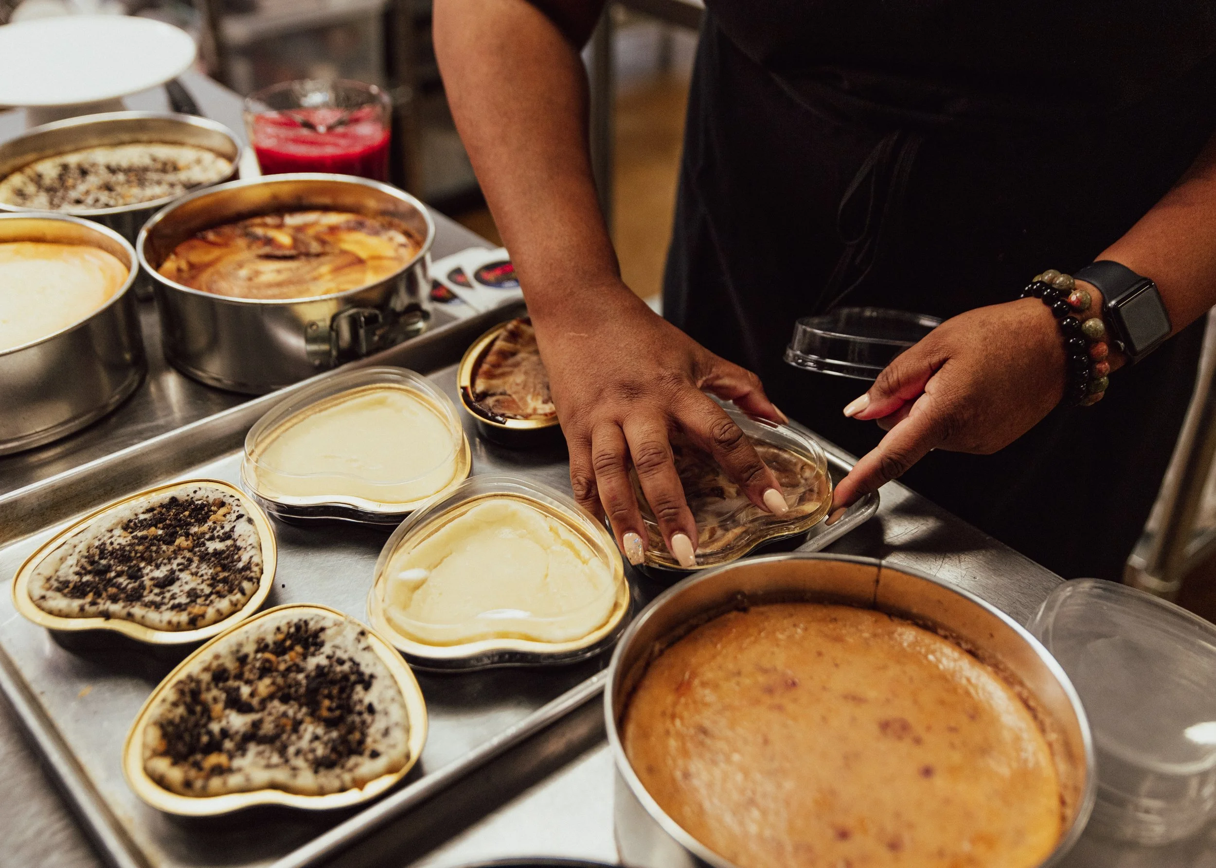 Person preparing and arranging heart-shaped desserts with various toppings on a tray in a kitchen.