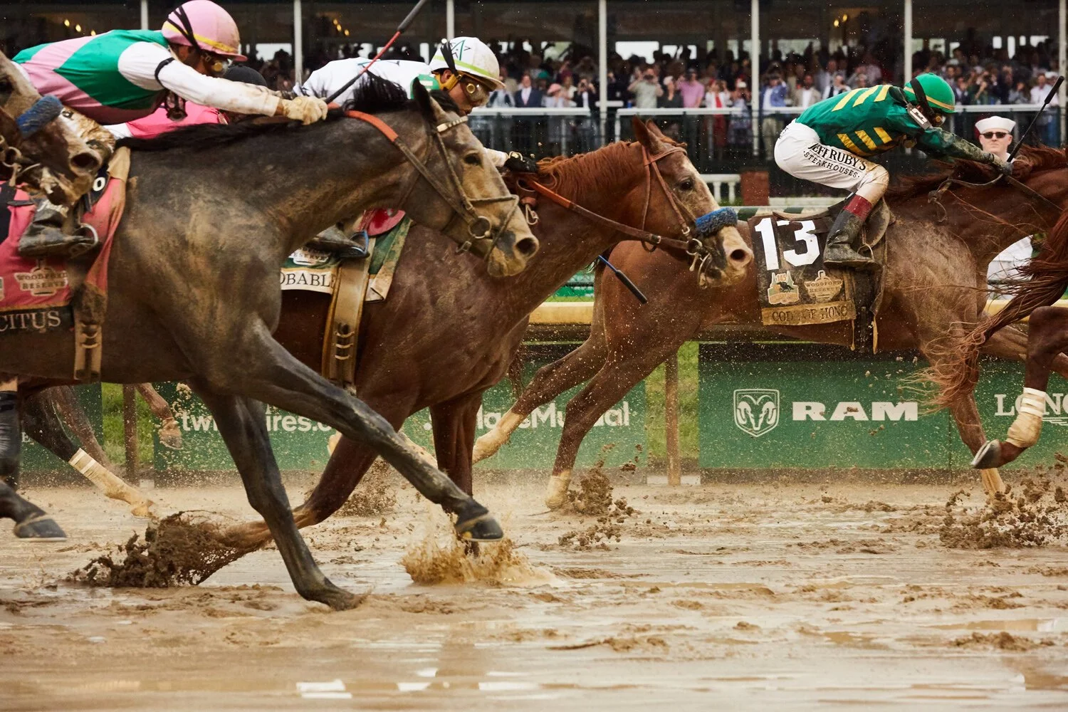 Horse race with jockeys riding thoroughbreds on a dirt track, with spectators in the background.