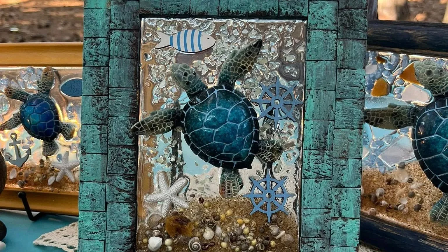 A decorative glass art piece featuring a sea turtle, starfish, and nautical elements, set within a weathered turquoise frame.