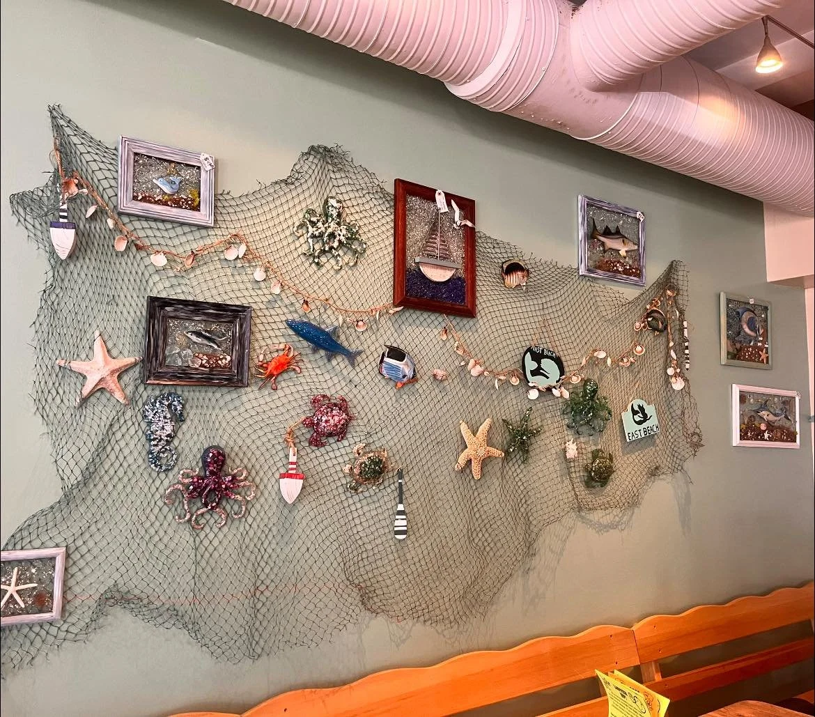Decorative wall with fishing net, picture frames, shells, starfish, octopus, seaweed, and nautical signs.