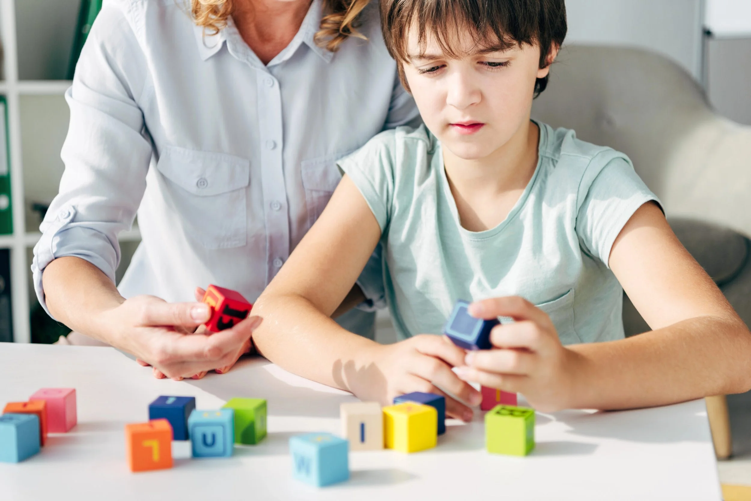 A young boy and an adult woman working together with colorful alphabet blocks on a table.