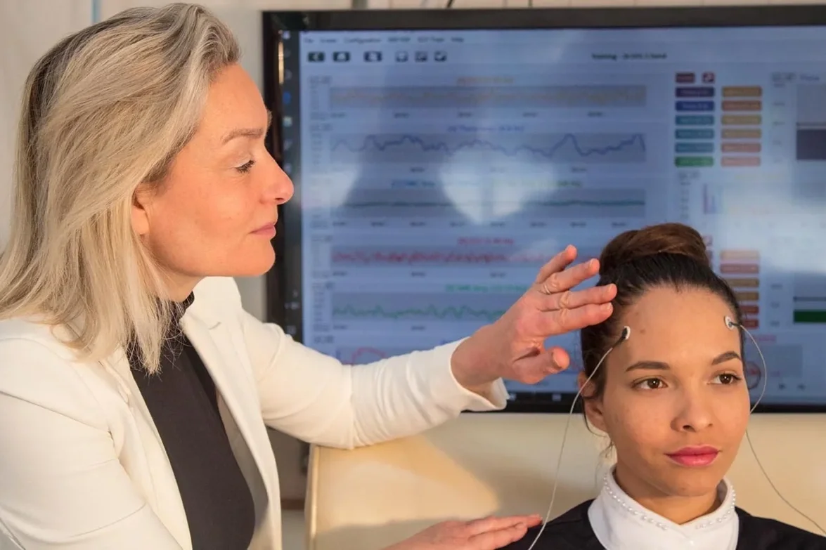 Doctor performing a brain activity test with EEG wires on a woman's head in a medical office.