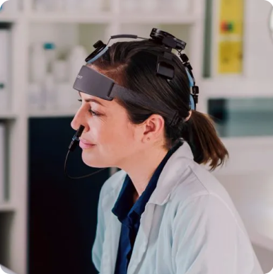 Woman in a lab coat wearing a headgear with attached equipment, working in a laboratory.