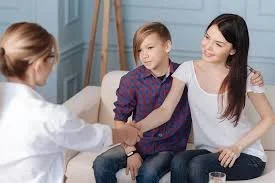 A woman and a young boy sitting on a couch talking to a doctor in a white coat.