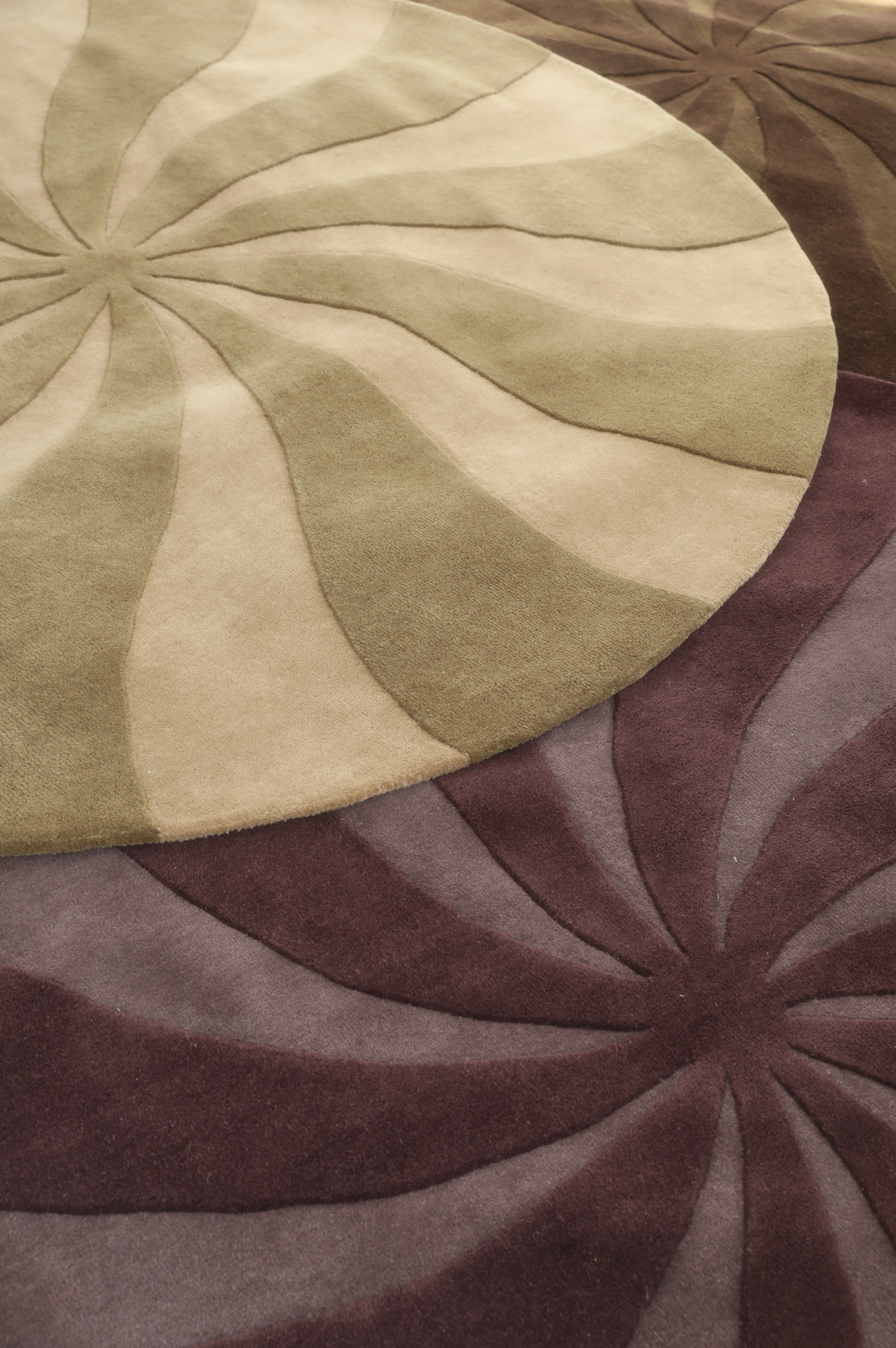 Close-up of overlapping circular rugs with flower petal patterns in beige, green, and maroon colors.