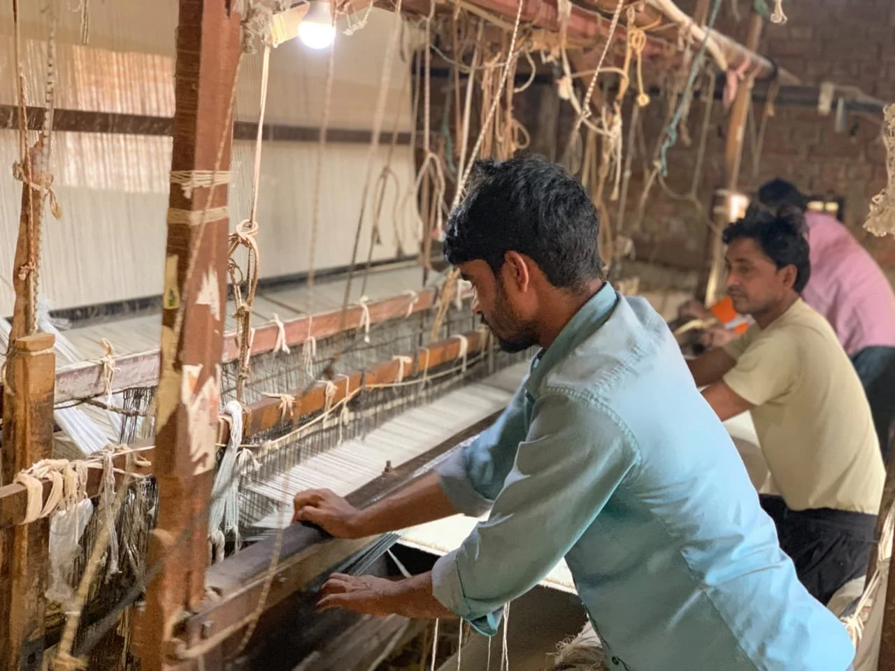 Men working on a traditional handloom weaving machine in a workshop.