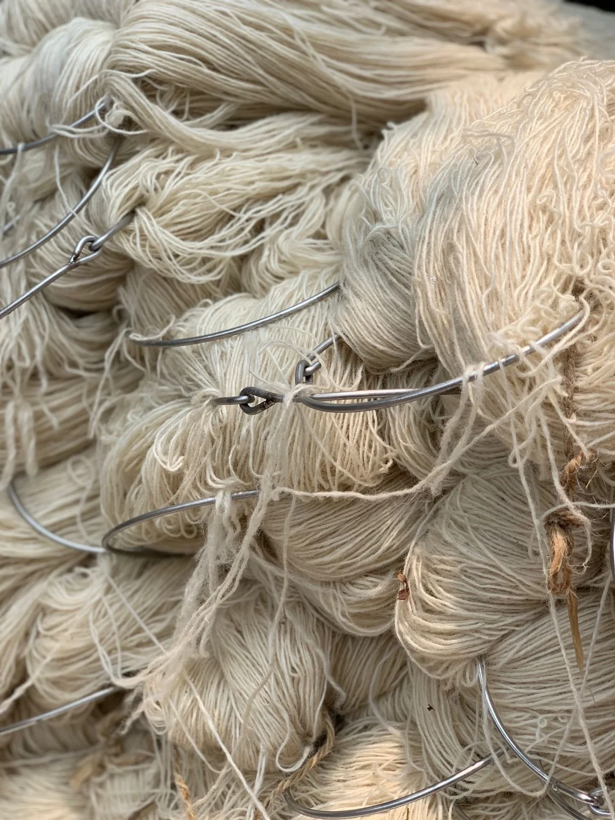 Close-up of skeins of natural-colored yarn or thread intertwined with metal wire.