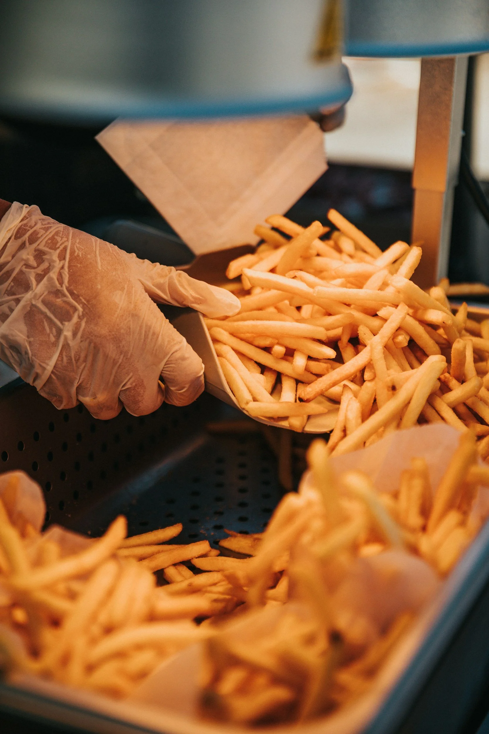 A person wearing gloves is scooping French fries from a tray.