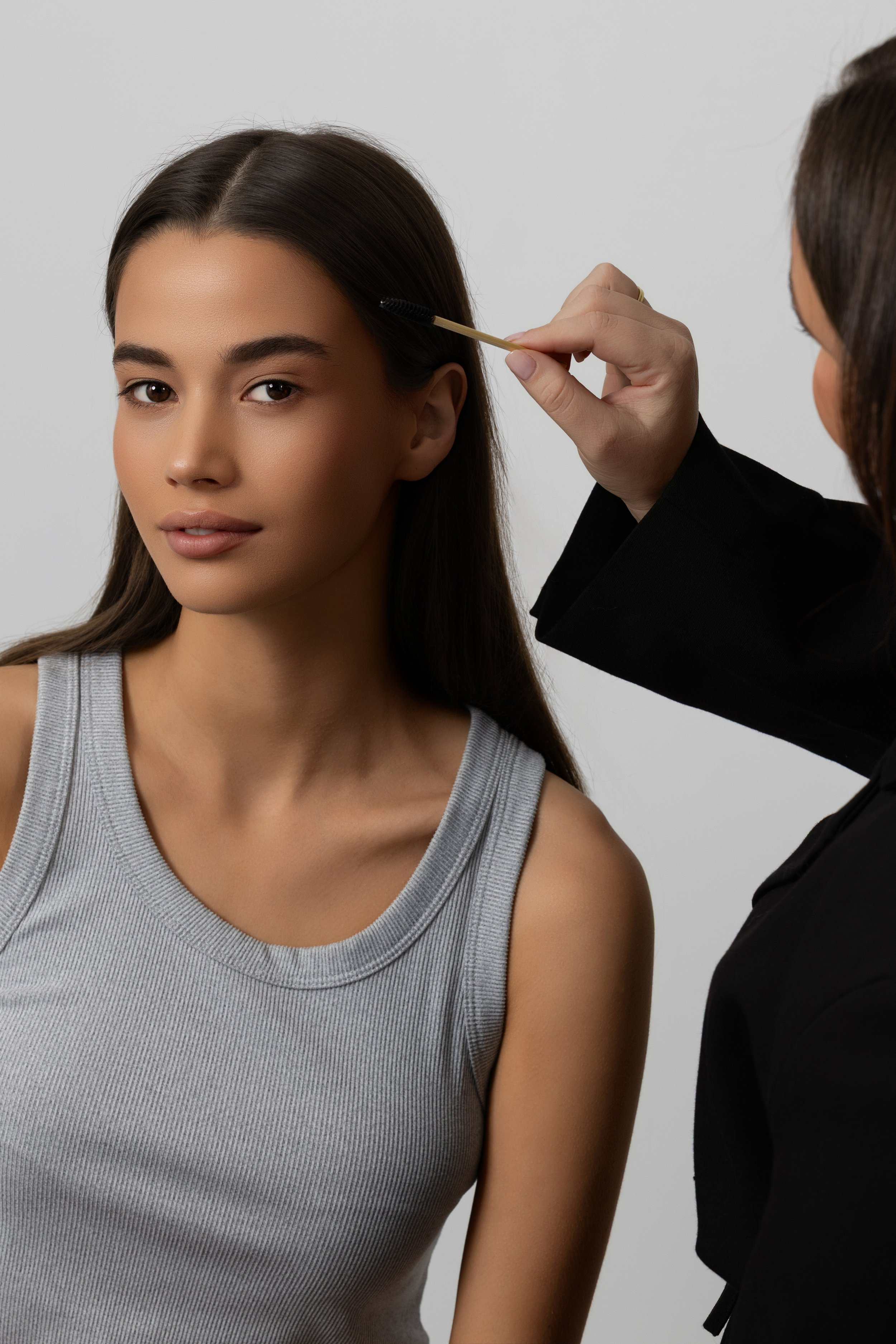 A woman in a gray tank top receiving a shot in her upper arm from a healthcare professional wearing a black jacket.