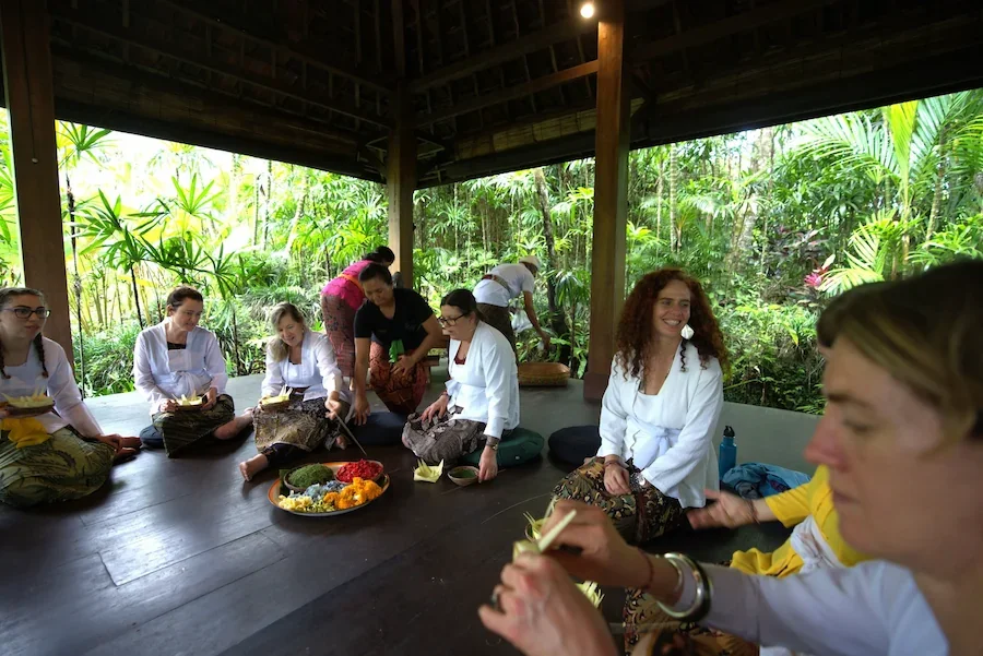 Retreat participants making traditional Balinese flower offerings with local Balinese women during the somatic healing retreat