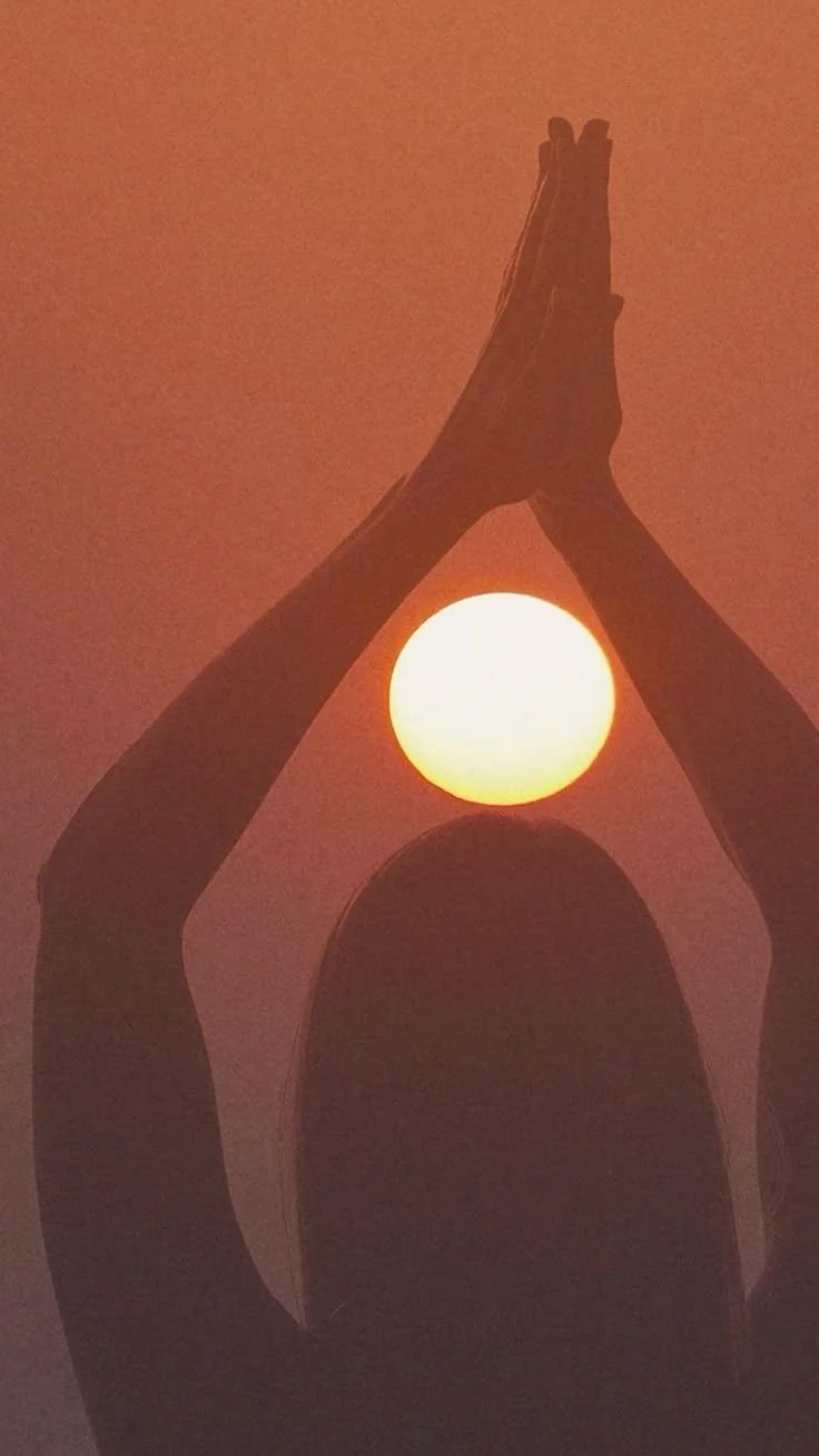 A person standing with hands pressed together in a prayer position, silhouetted against a sunset, with the sun positioned between their hands.
