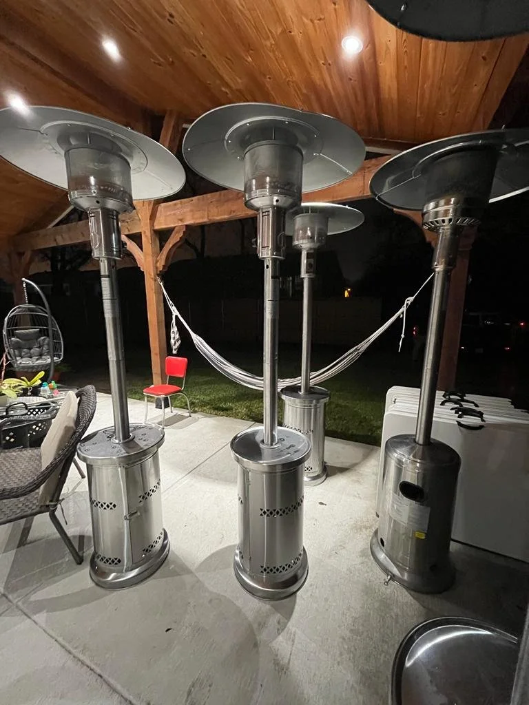 Three outdoor patio heaters with large reflective tops arranged under a wooden porch ceiling at night.