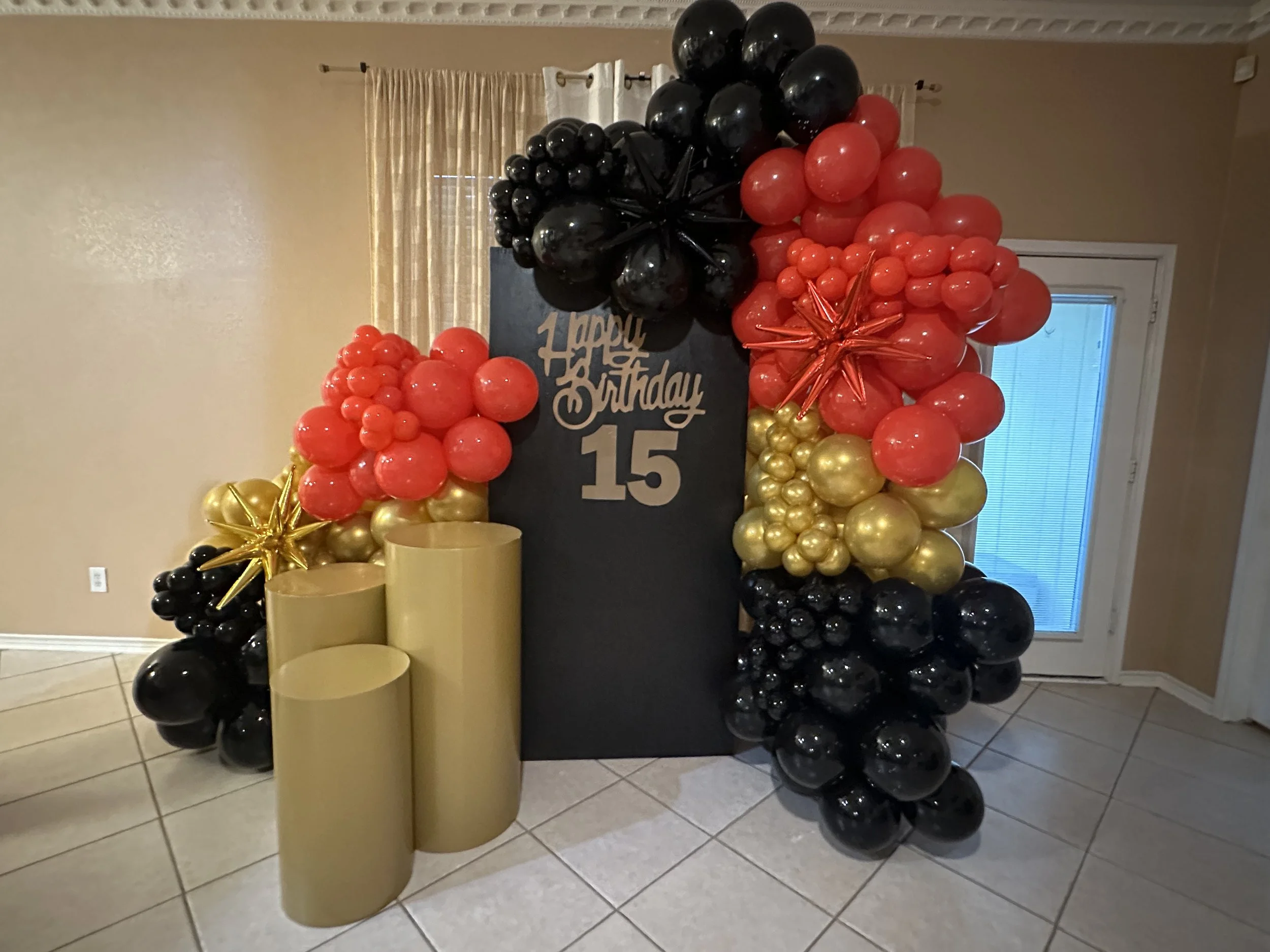Decoration with black, red, and gold balloons surrounding a sign that says 'Happy 15th Birthday'.