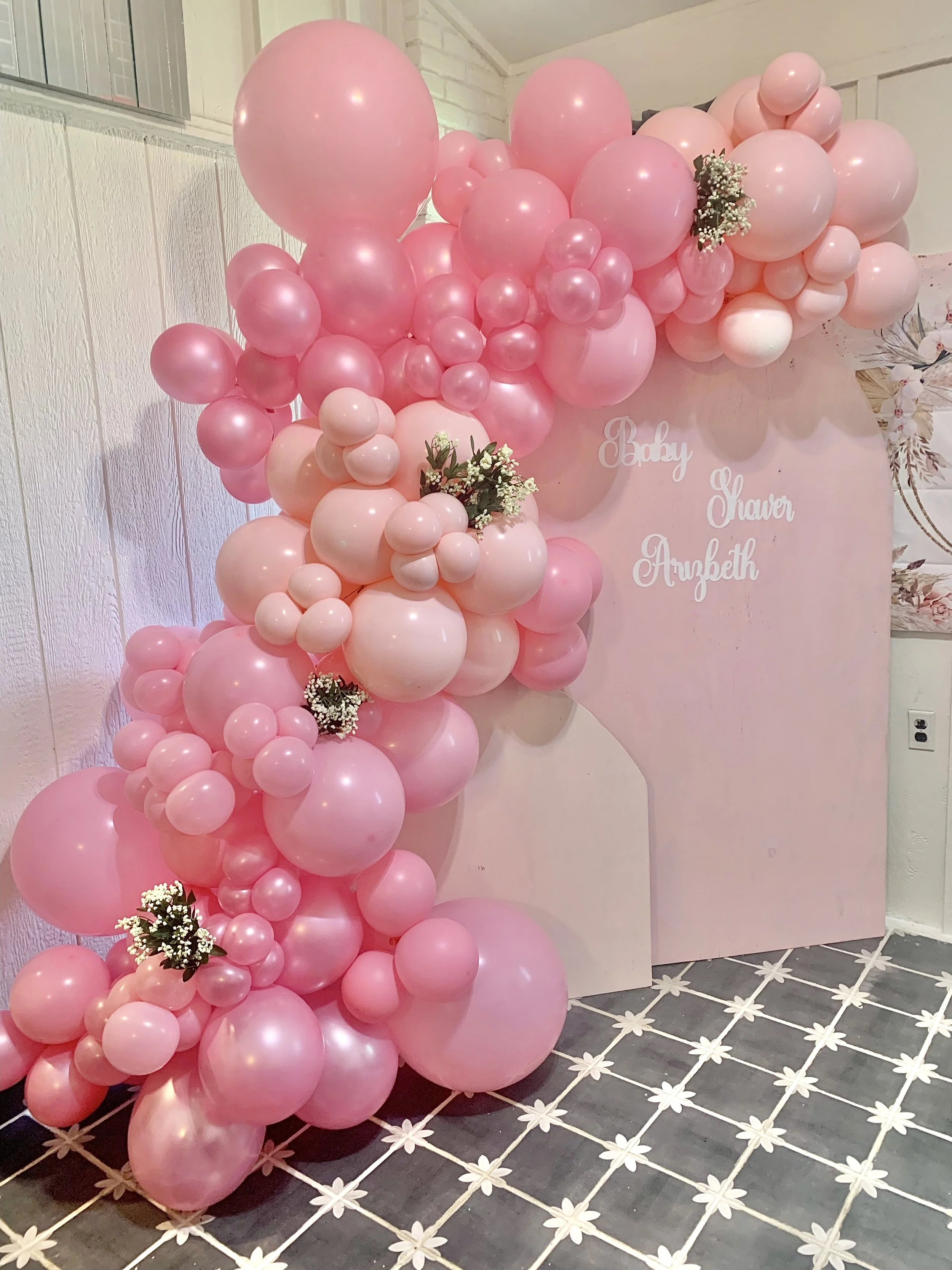 A pink balloon arrangement with various sizes of balloons, some with flowers, set against a pink backdrop with white text that reads 'Baby Shower Elizabeth'.