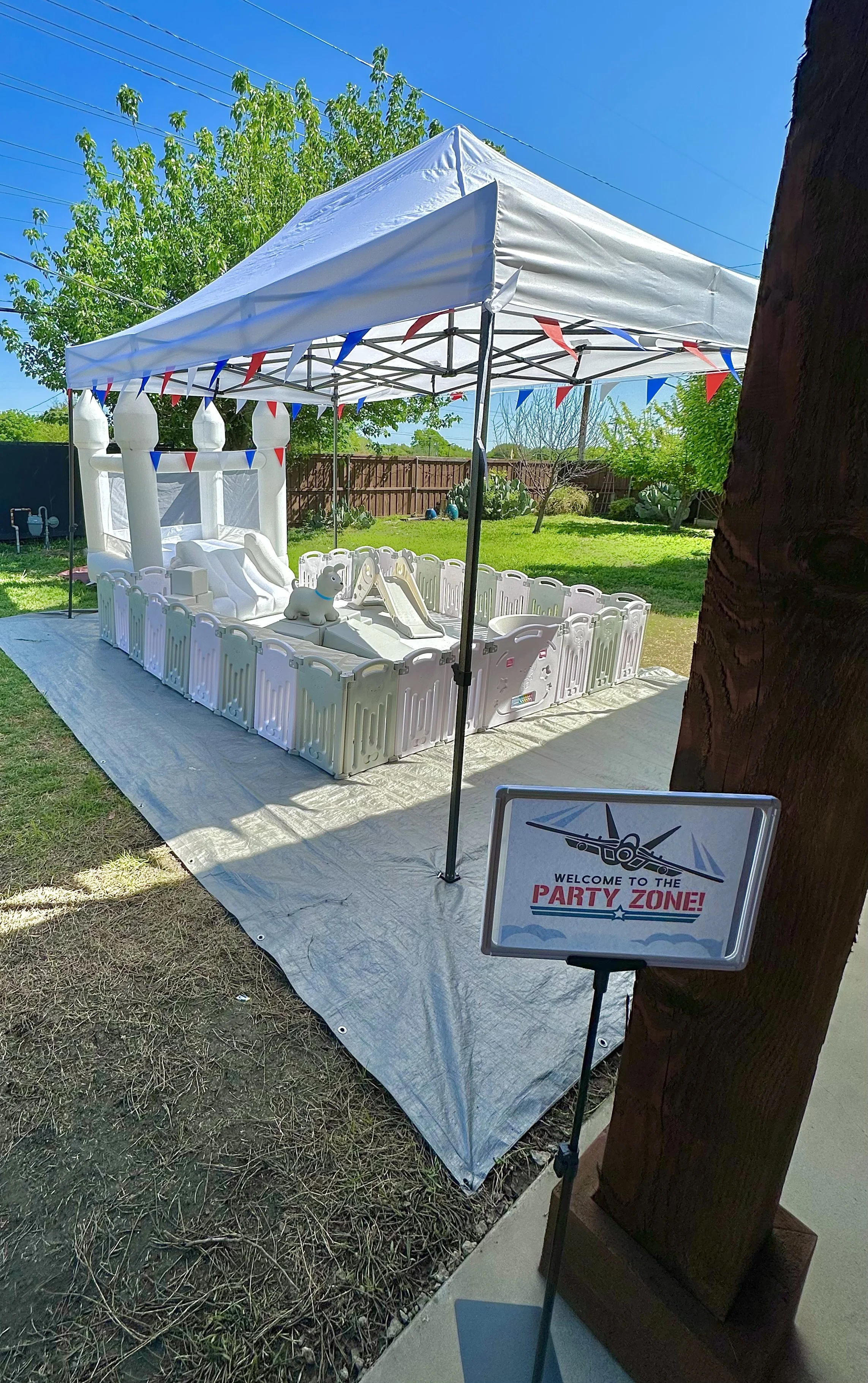 Outdoor party setup with a white tent, red and blue bunting, a small inflatable slide, and a sign that reads 'Welcome to the Party Zone.'