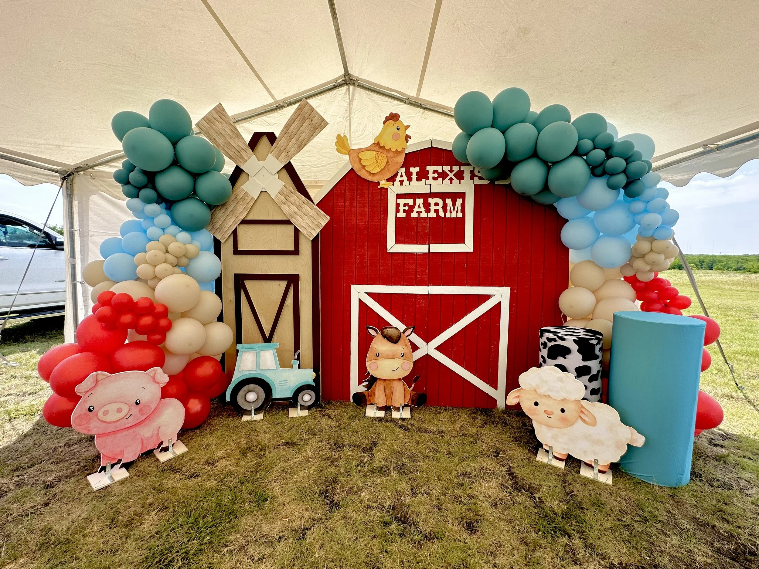 Decorative farm-themed display with balloons, cartoon farm animals, a windmill, barn, and a small tractor.