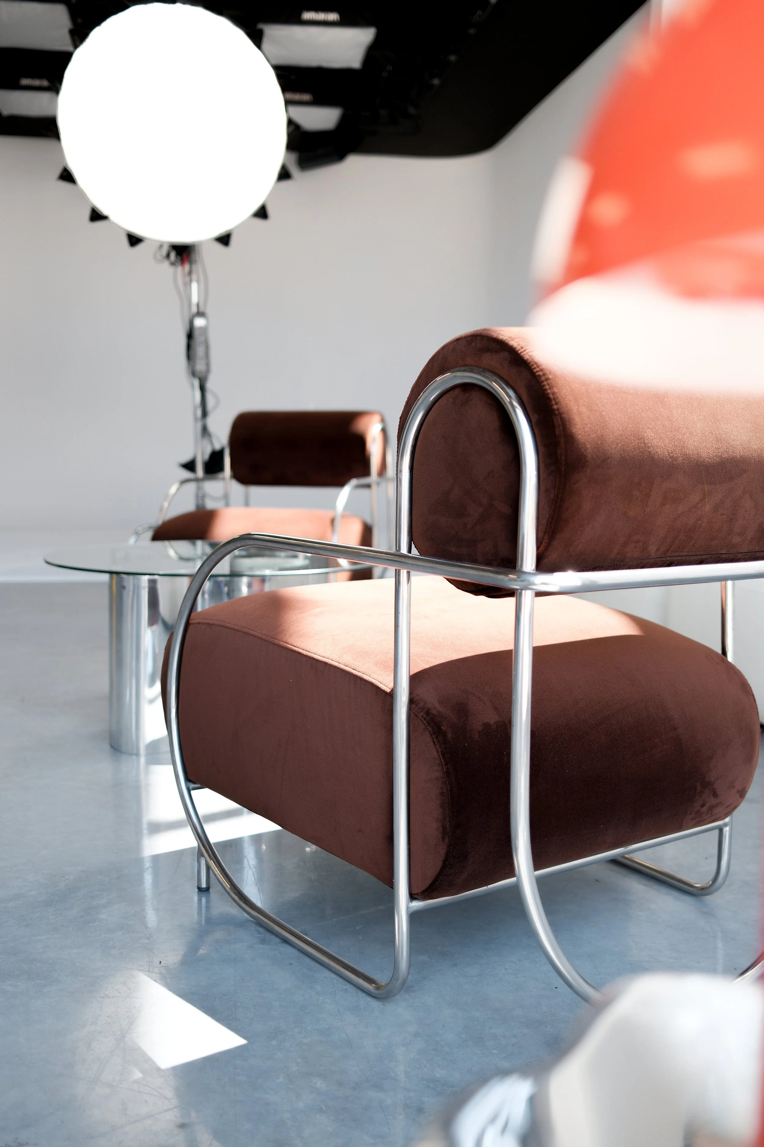 Modern studio setting in Newcastle with brown velvet chairs featuring chrome frames, a small glass table, and studio lighting equipment in the background.