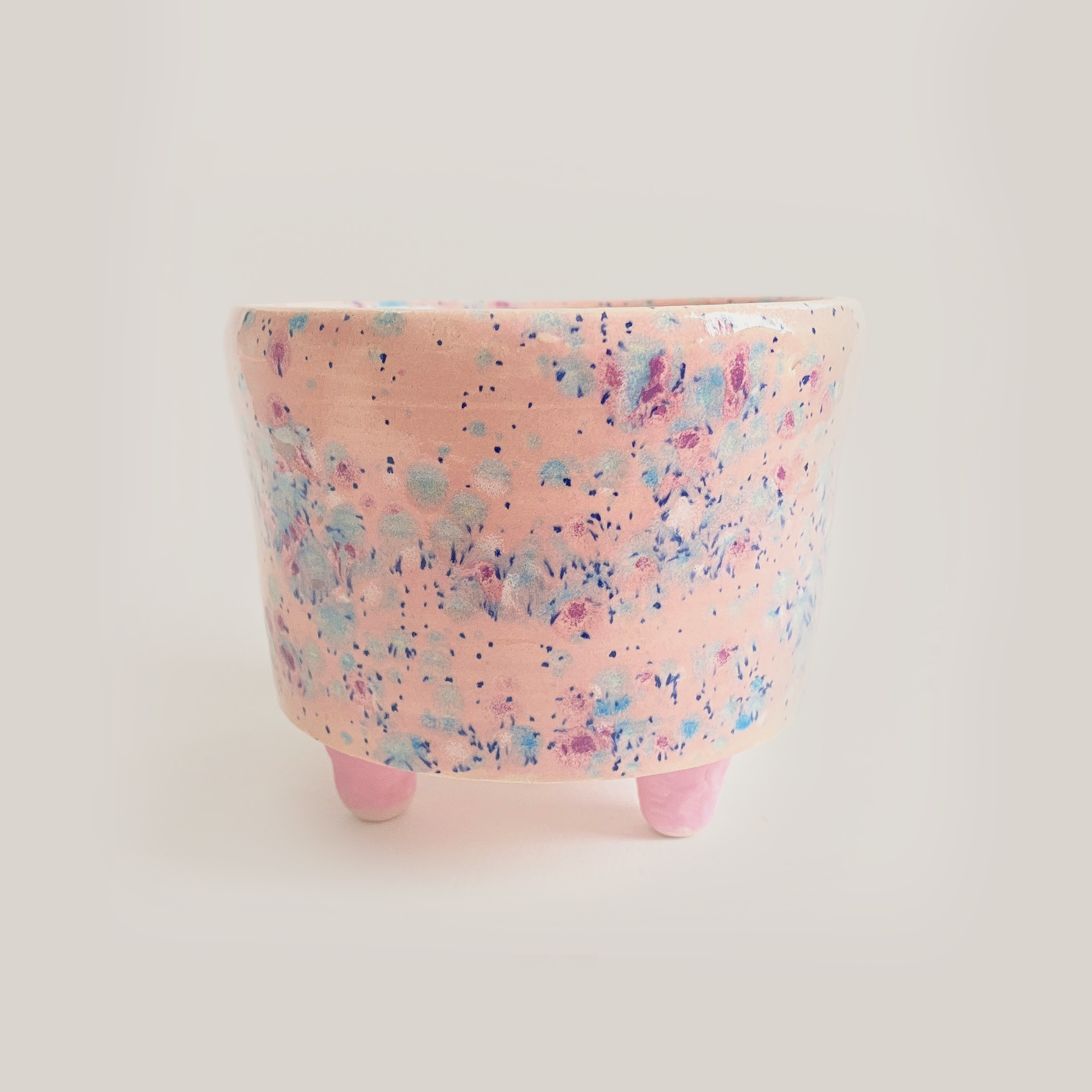 ceramic planter with pink stubs as feet and glazed in a pink speckled glaze that resembles sprinkles.