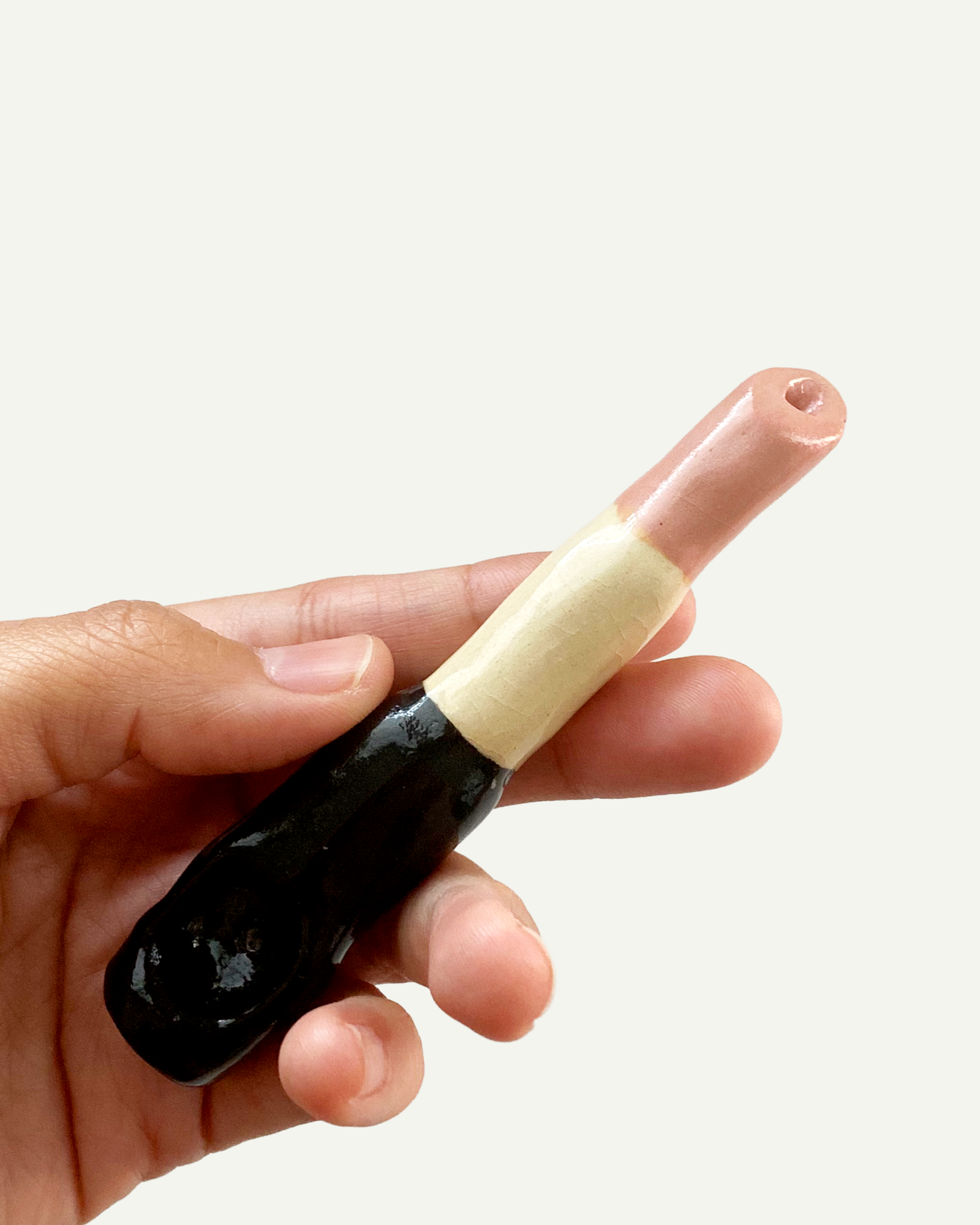 hand holding a ceramic pipe in the form of pink lipstick.