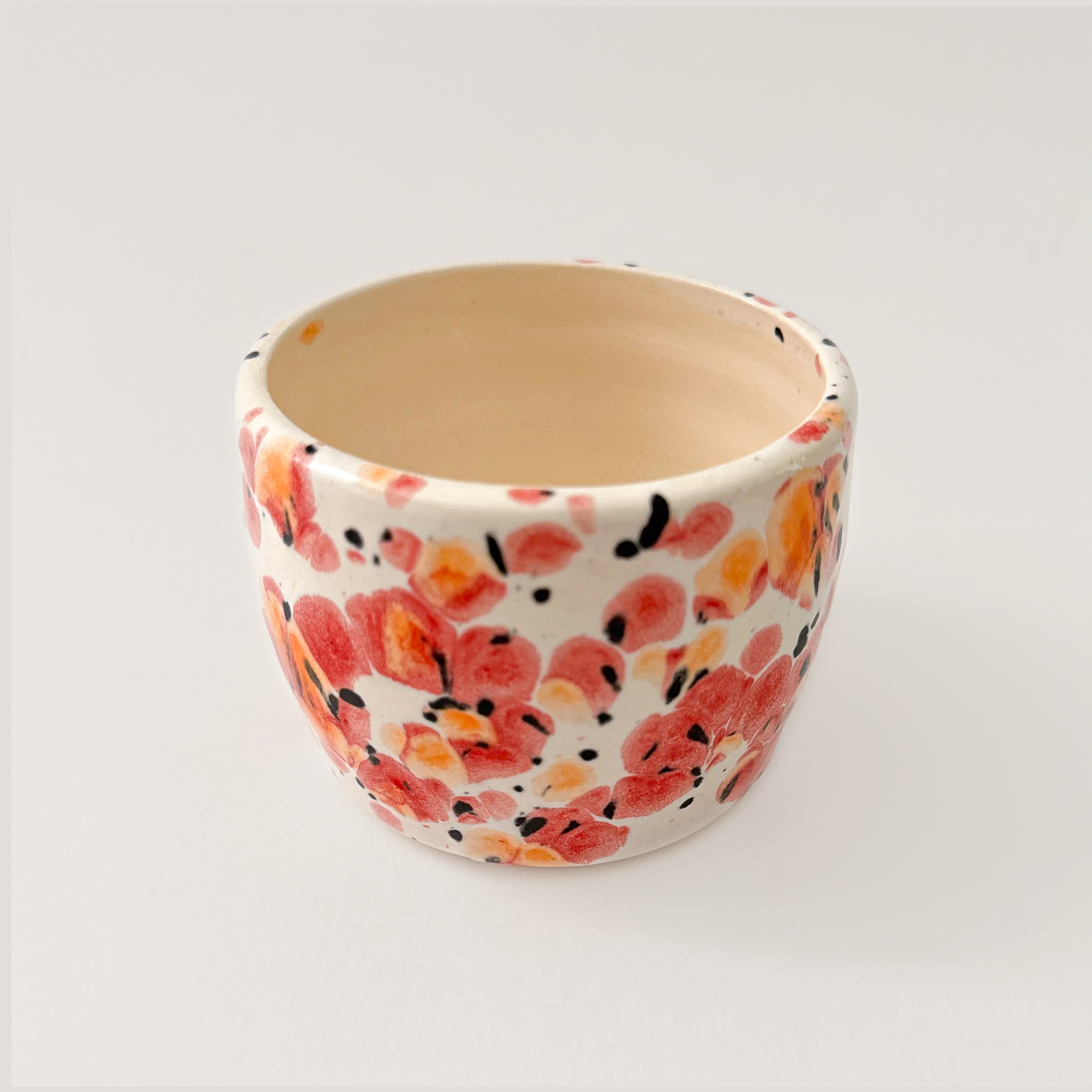 Speckled red orange and black glaze on small cream colored cup.