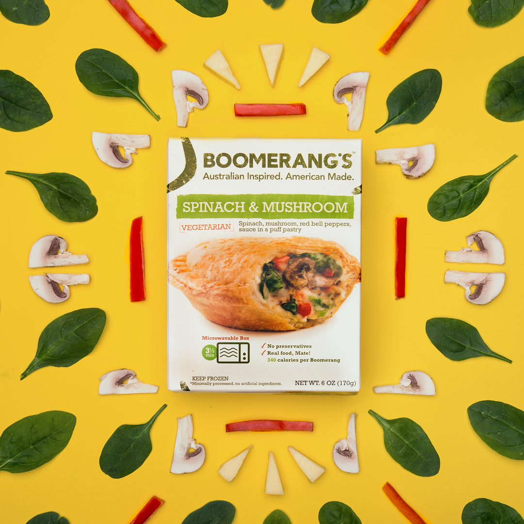 Boomerang's pies box with cut up mushrooms, peppers, cheese and spinach leaves creating a knolled pattern on a yellow background