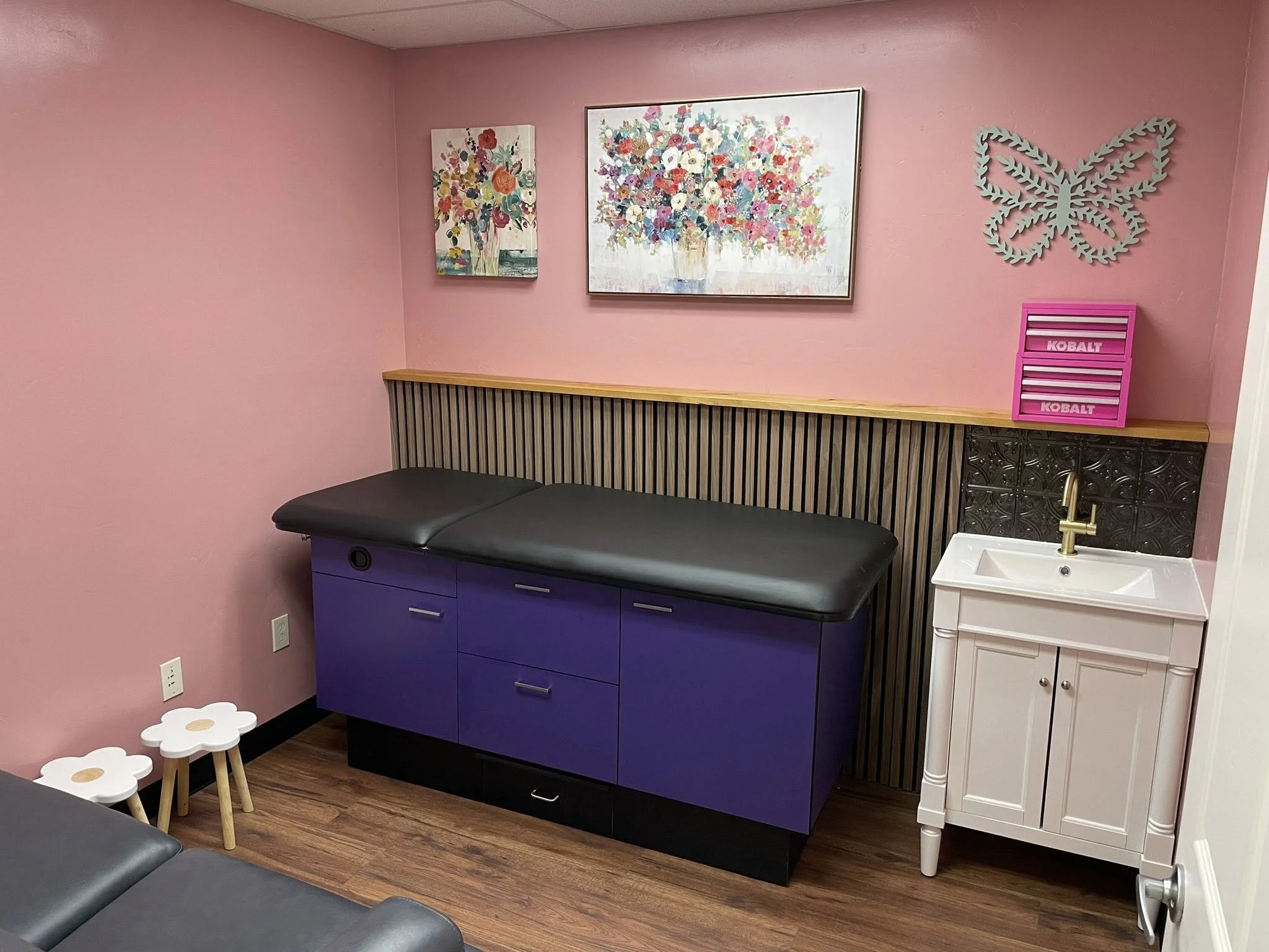 A bright and calming medical exam room at Restoration Health, featuring a clean, professional setup with soft pink accents designed to make patients feel at home.